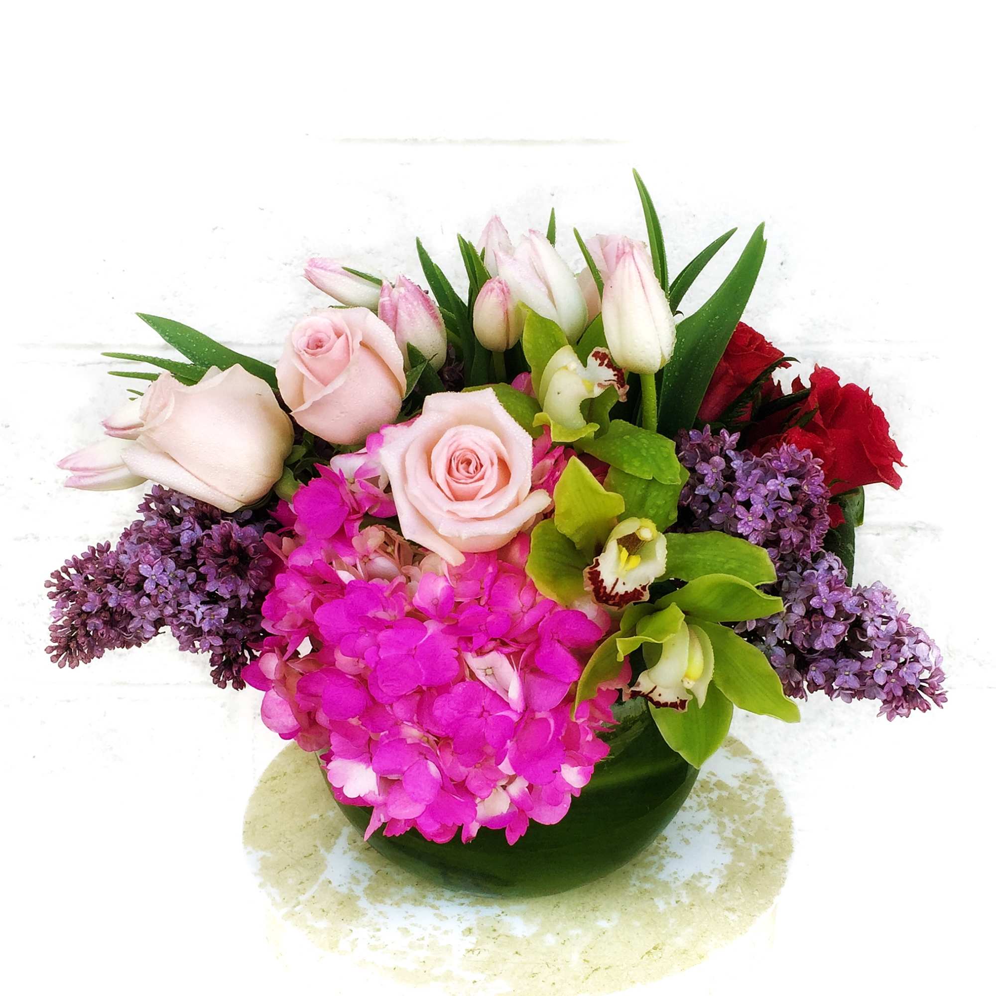 Mixed bouquet of pink roses, purple hydrangea, and orchids in a green vase