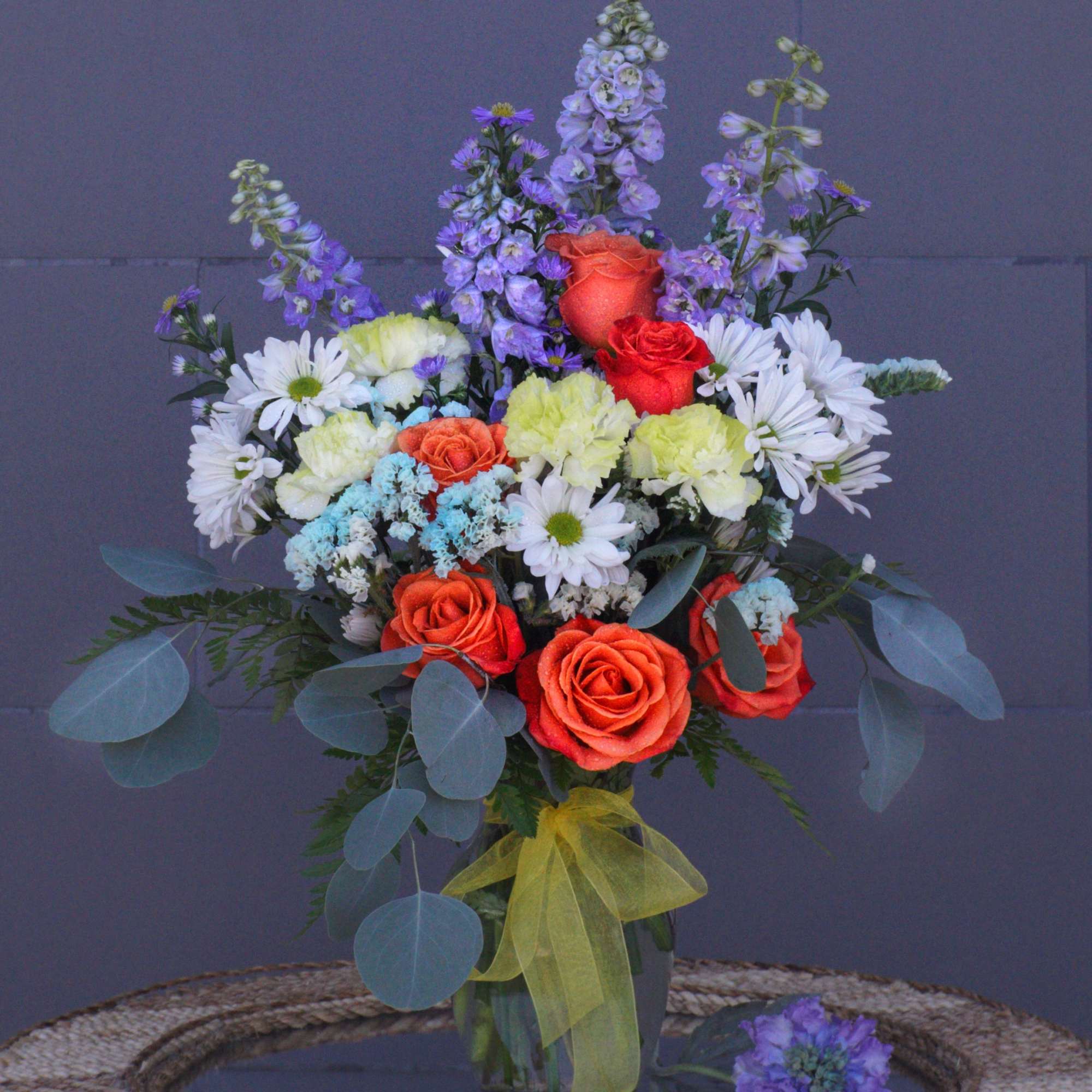 Bouquet of orange roses, white daisies, and purple flowers in a glass vase