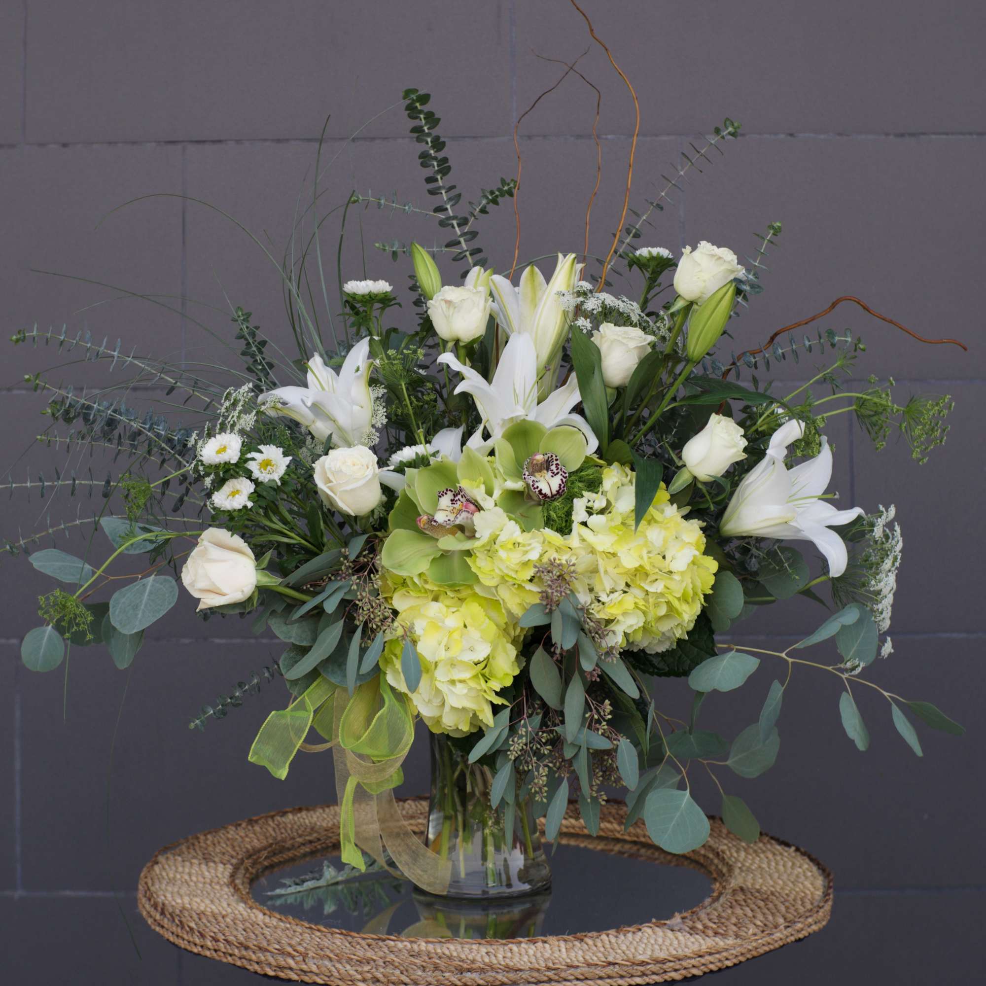 White lilies and roses in a glass vase with airy greenery