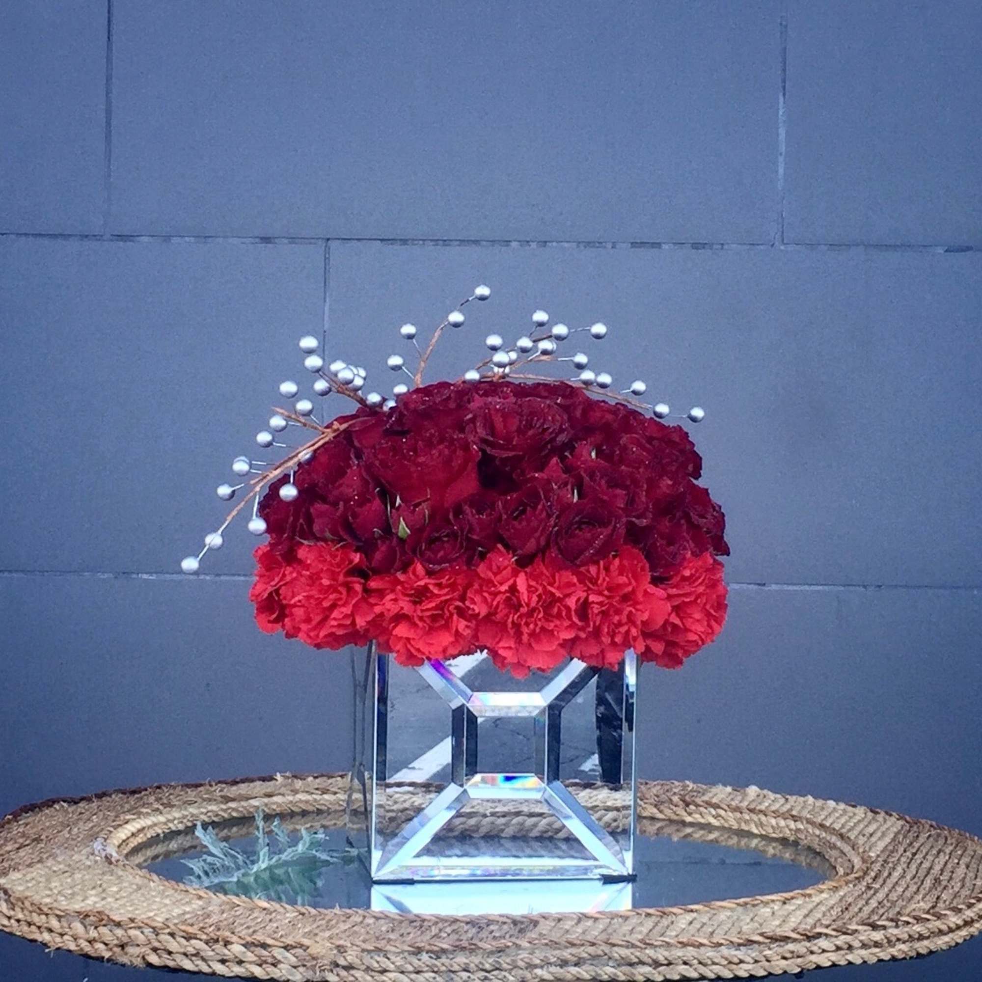 Red floral arrangement in a clear geometric vase with white berry accents
