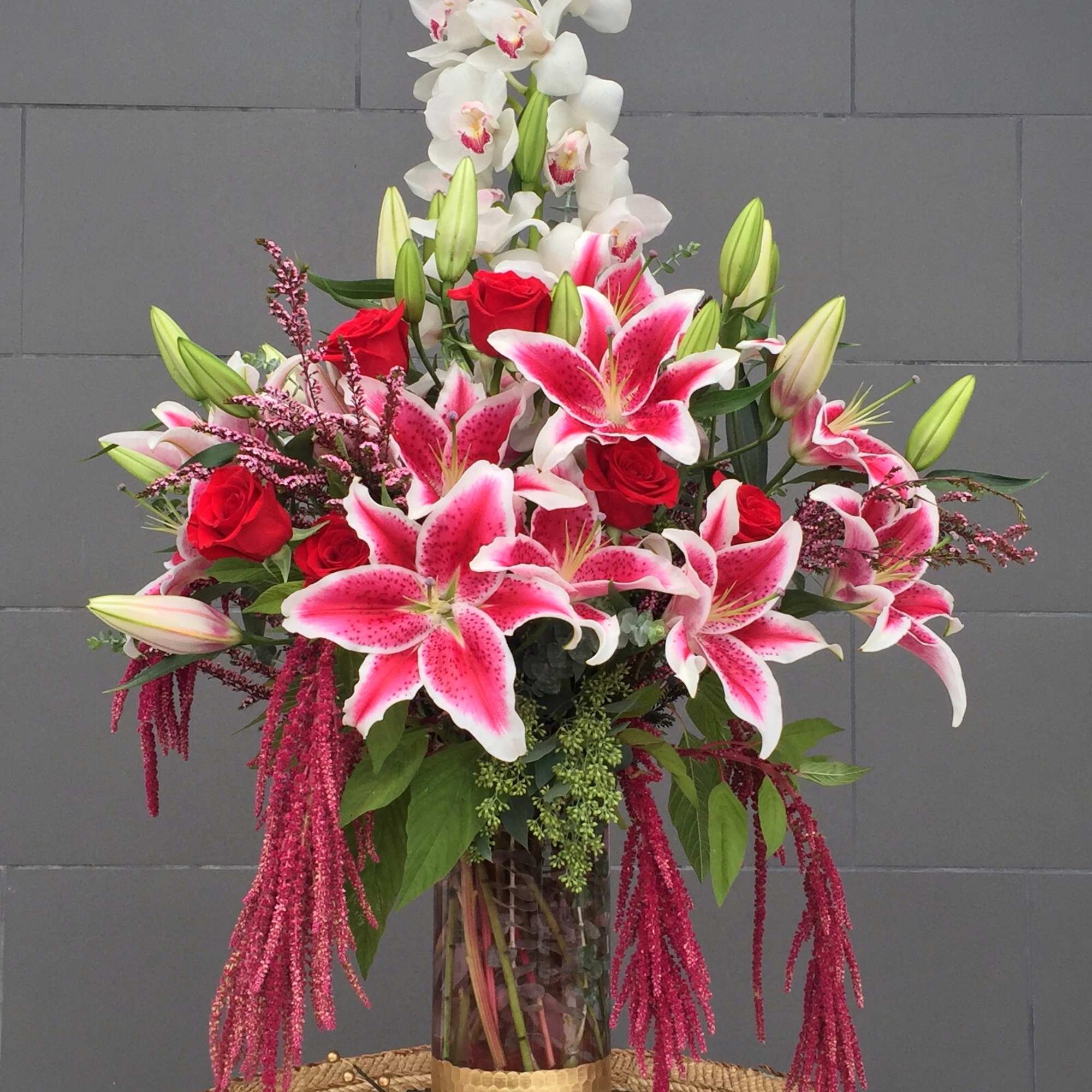 Tall bouquet of pink lilies, red roses, and white orchids in a glass vase