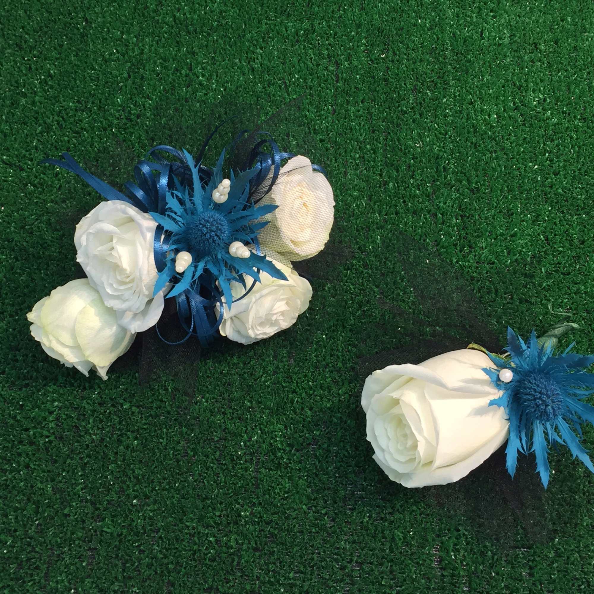 Two white rose boutonnieres with blue accents on green turf