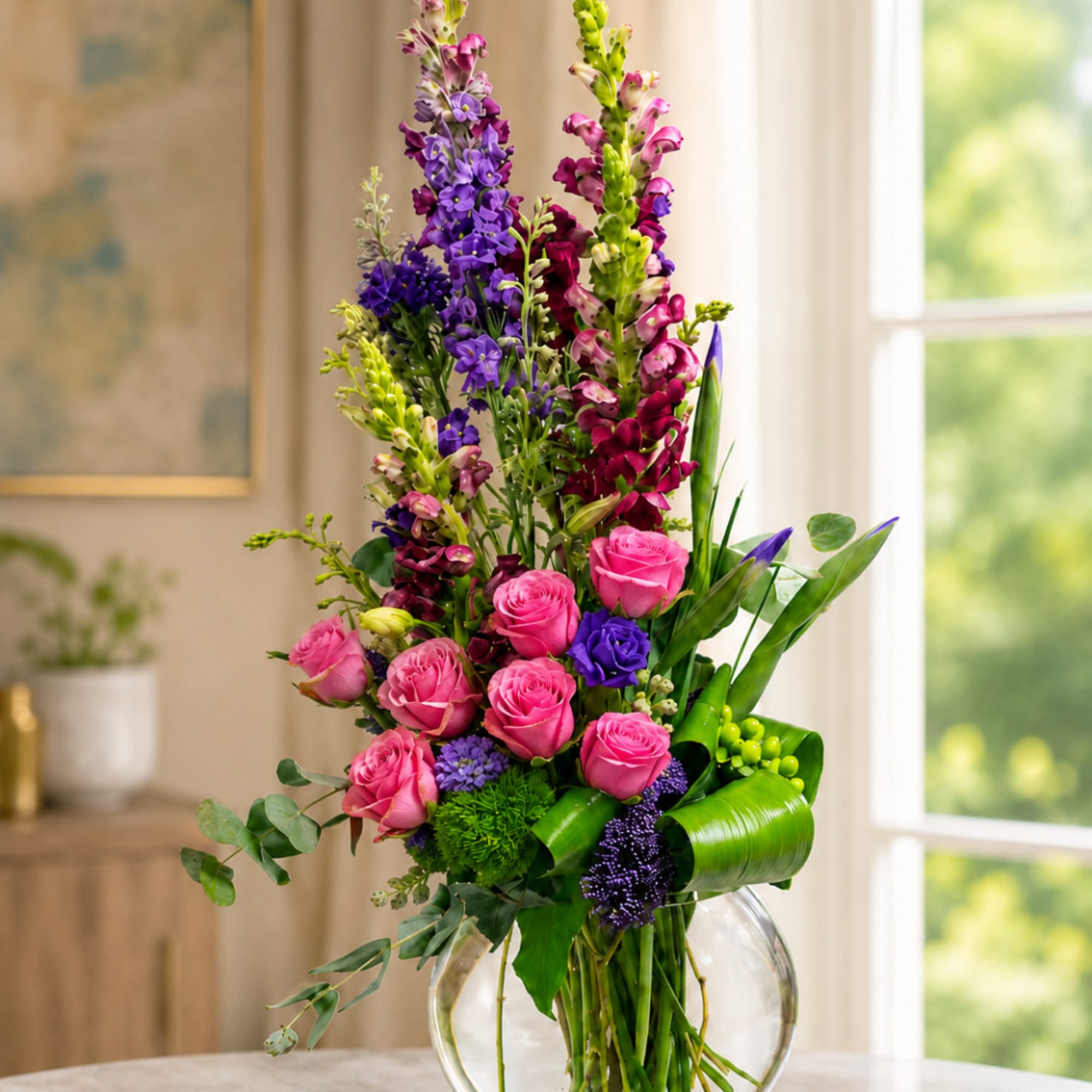 Tall bouquet of pink roses and purple flowers in a clear glass vase