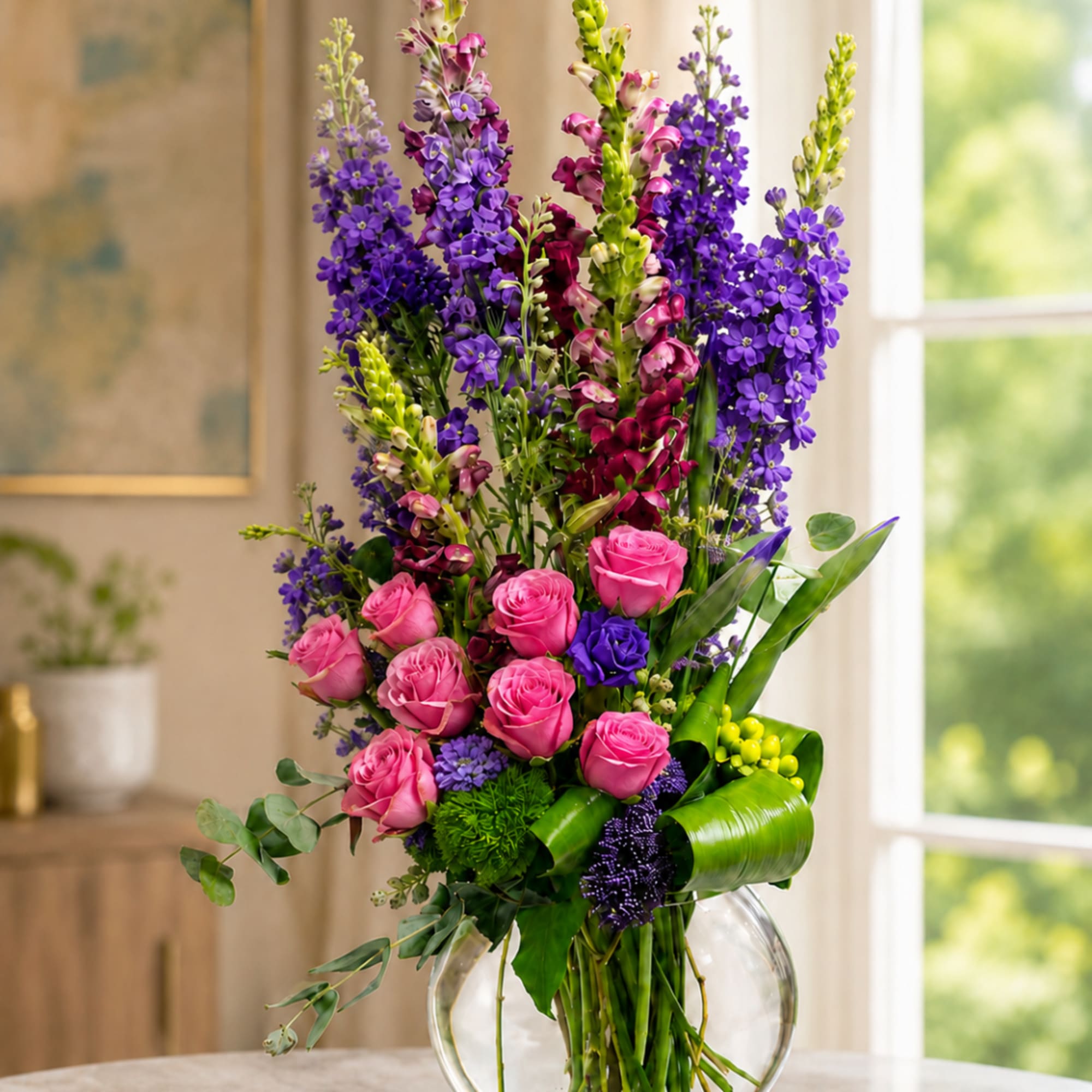 Tall bouquet of pink roses and purple flowers in a clear glass vase
