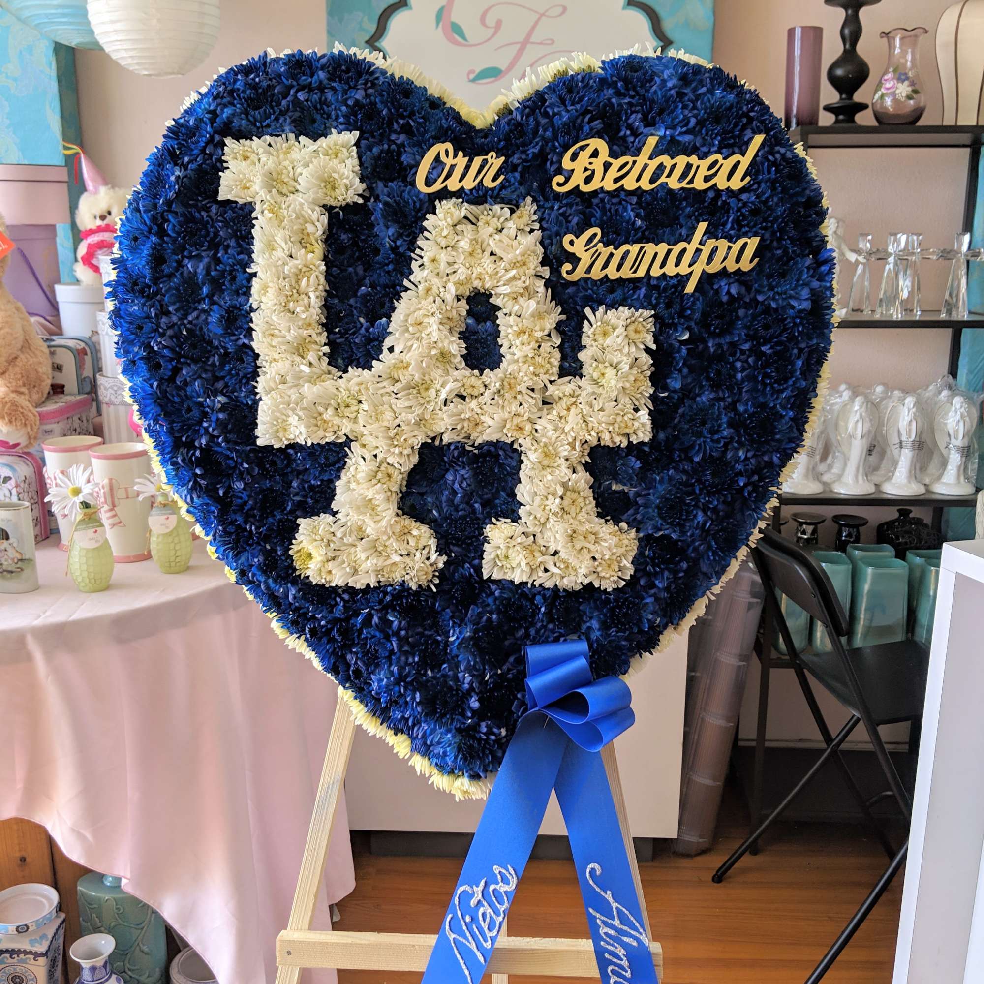 Heart-shaped floral tribute with blue and white flowers reading "Our Beloved Grandpa"