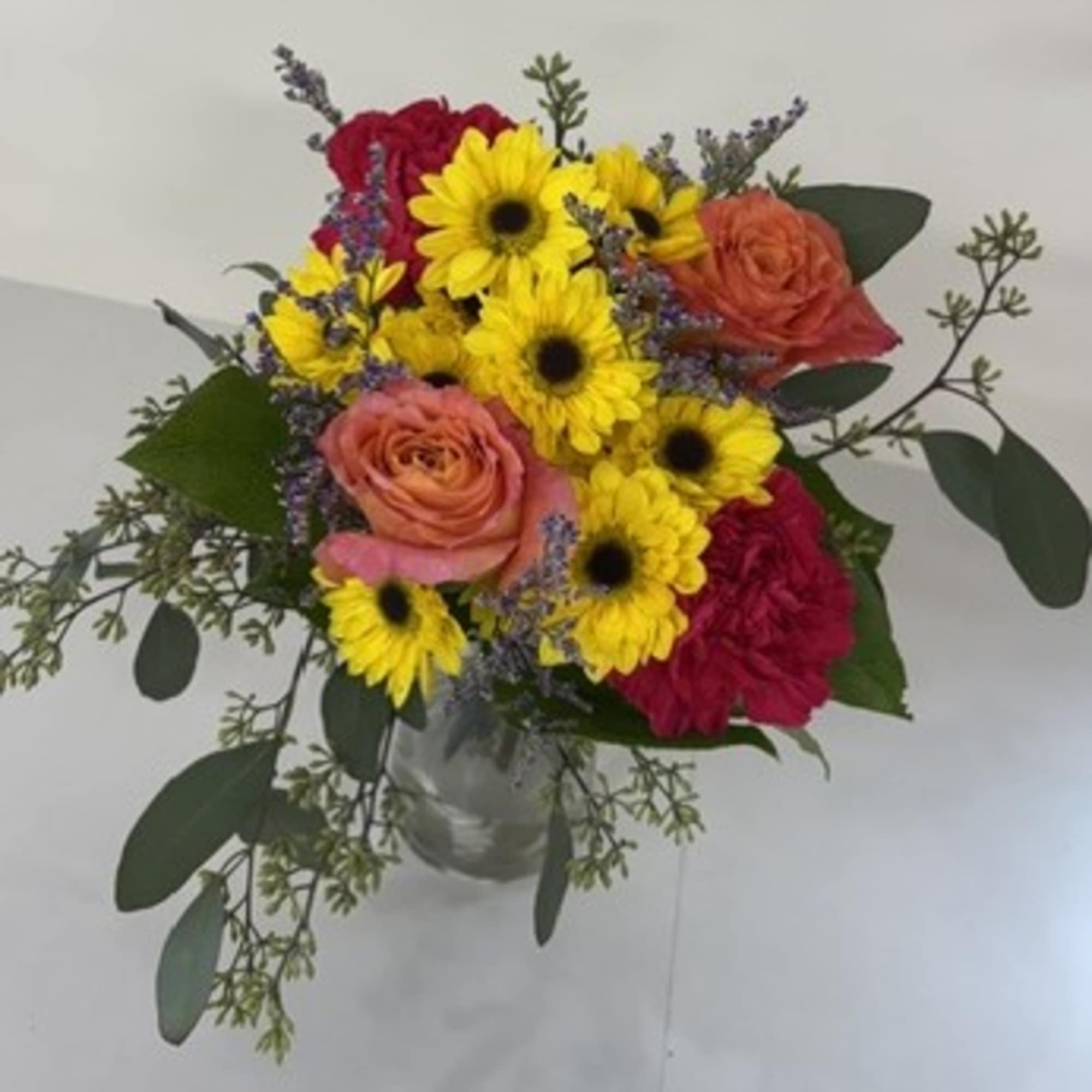 Bouquet of yellow daisies, pink roses, and red blooms in a glass vase