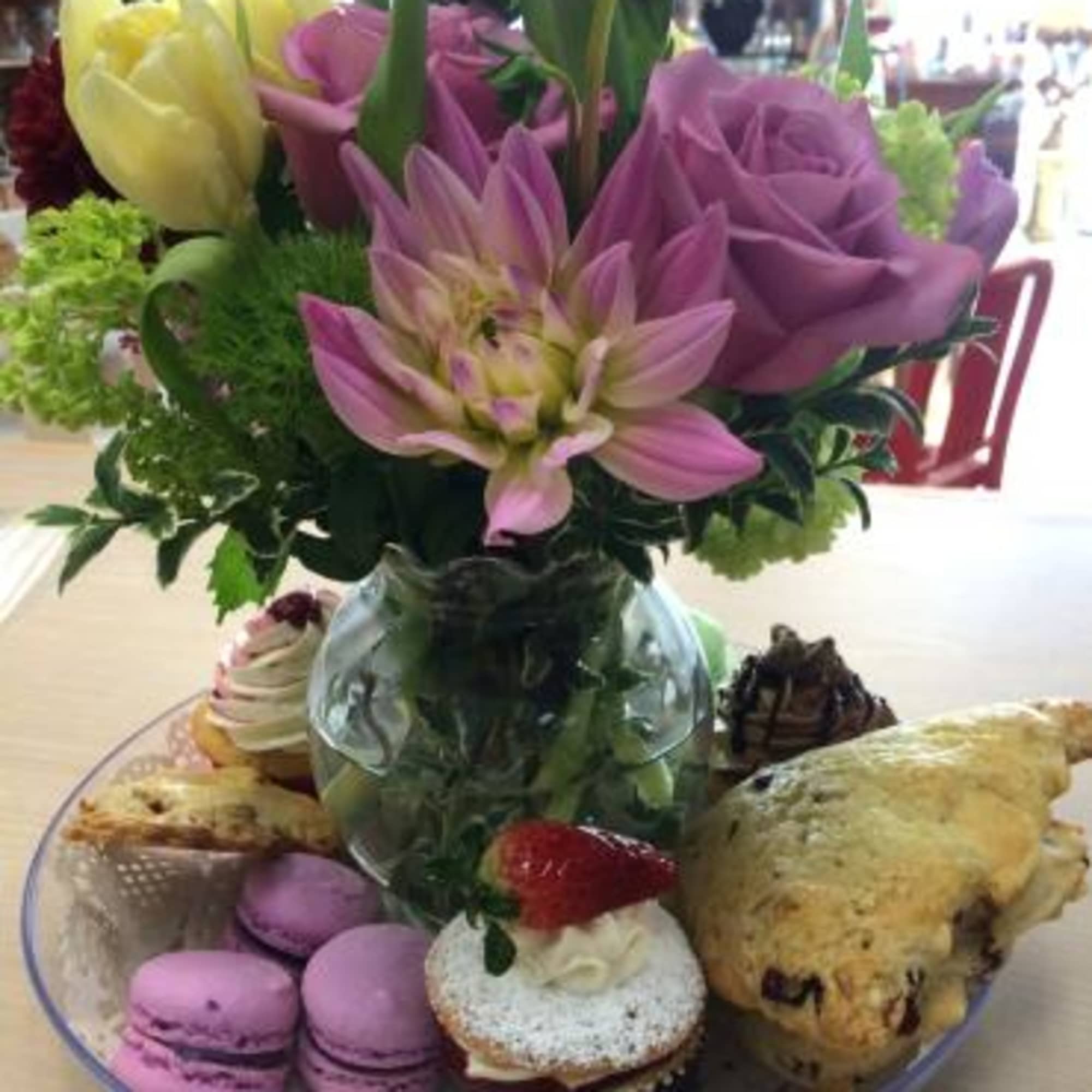 Flower arrangement in a glass vase surrounded by pastries and macarons
