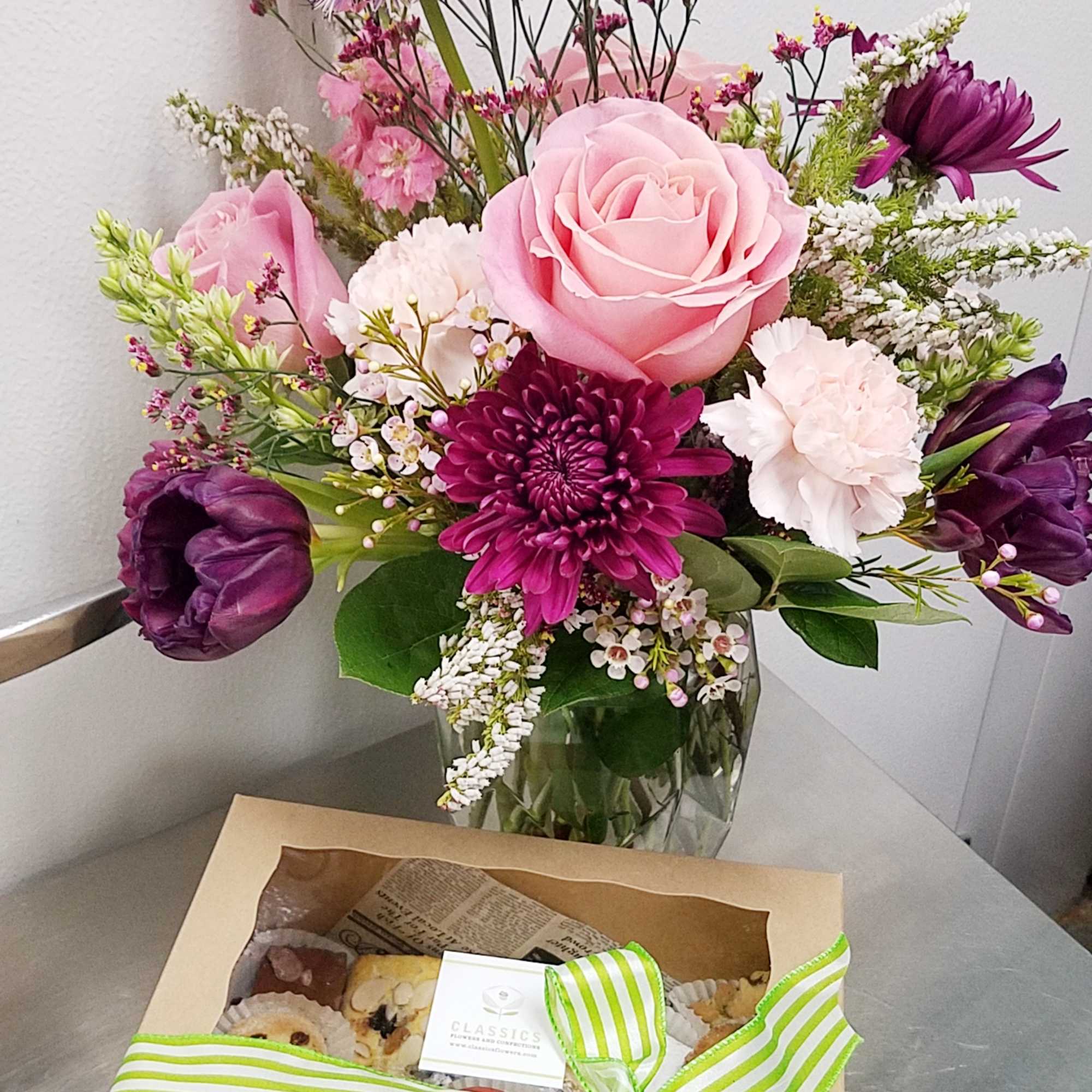 Pink and purple mixed bouquet in a glass vase with a pastry gift box in front
