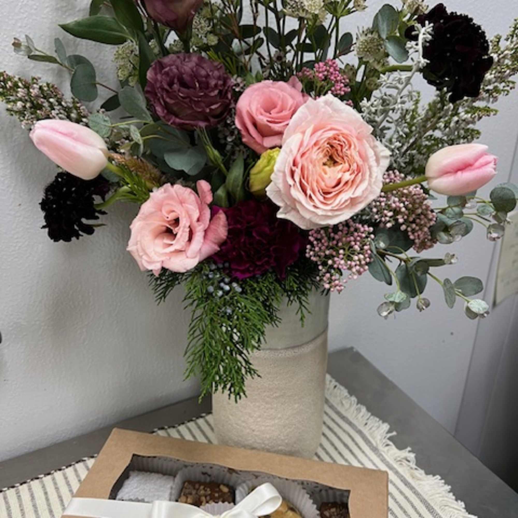 Mixed pink and burgundy bouquet in a tall vase with a box of macarons in front