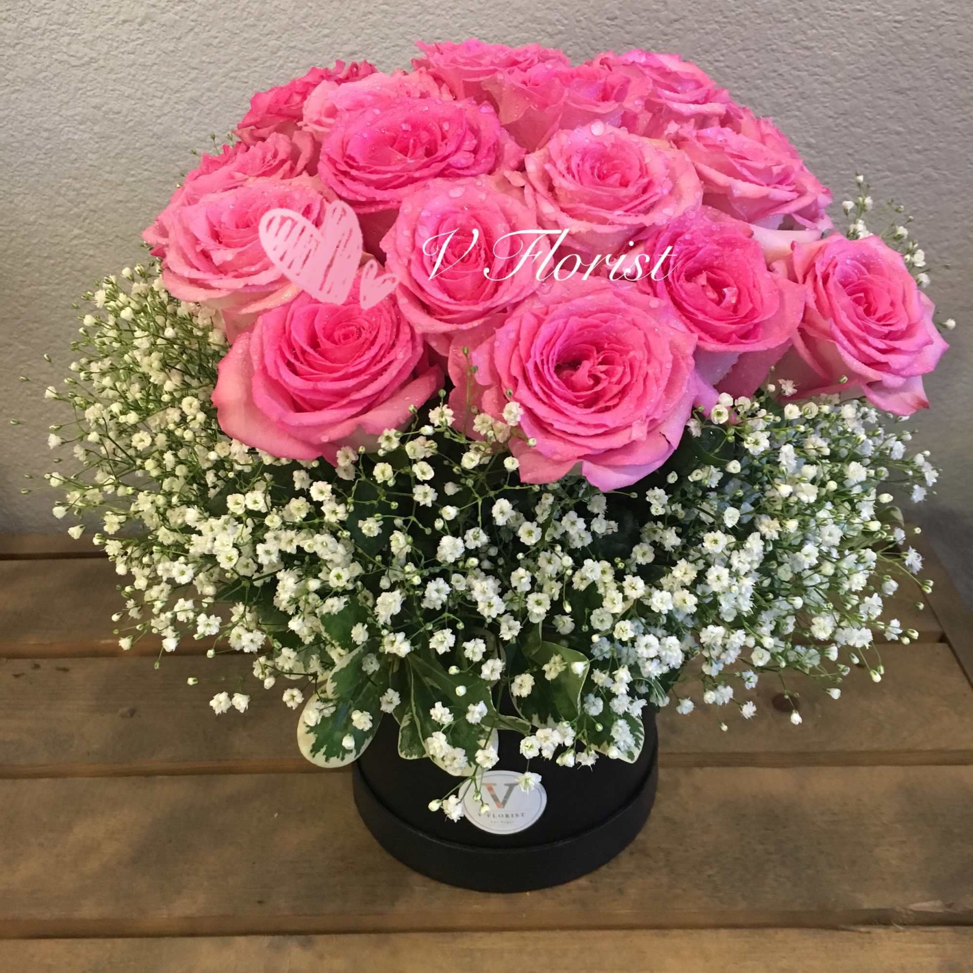 Round box arrangement of bright pink roses with white filler flowers in a black container