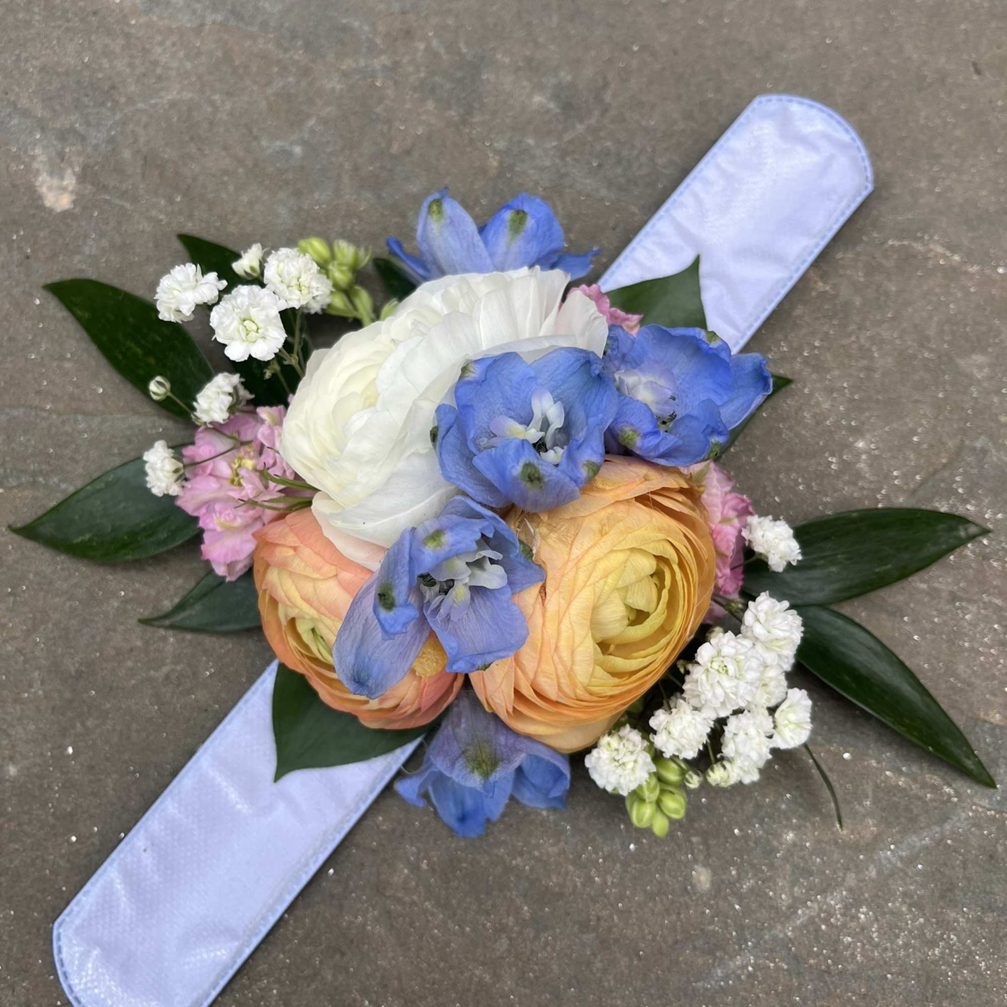 Hand-tied bouquet with blue, white, and peach flowers on a pale ribbon
