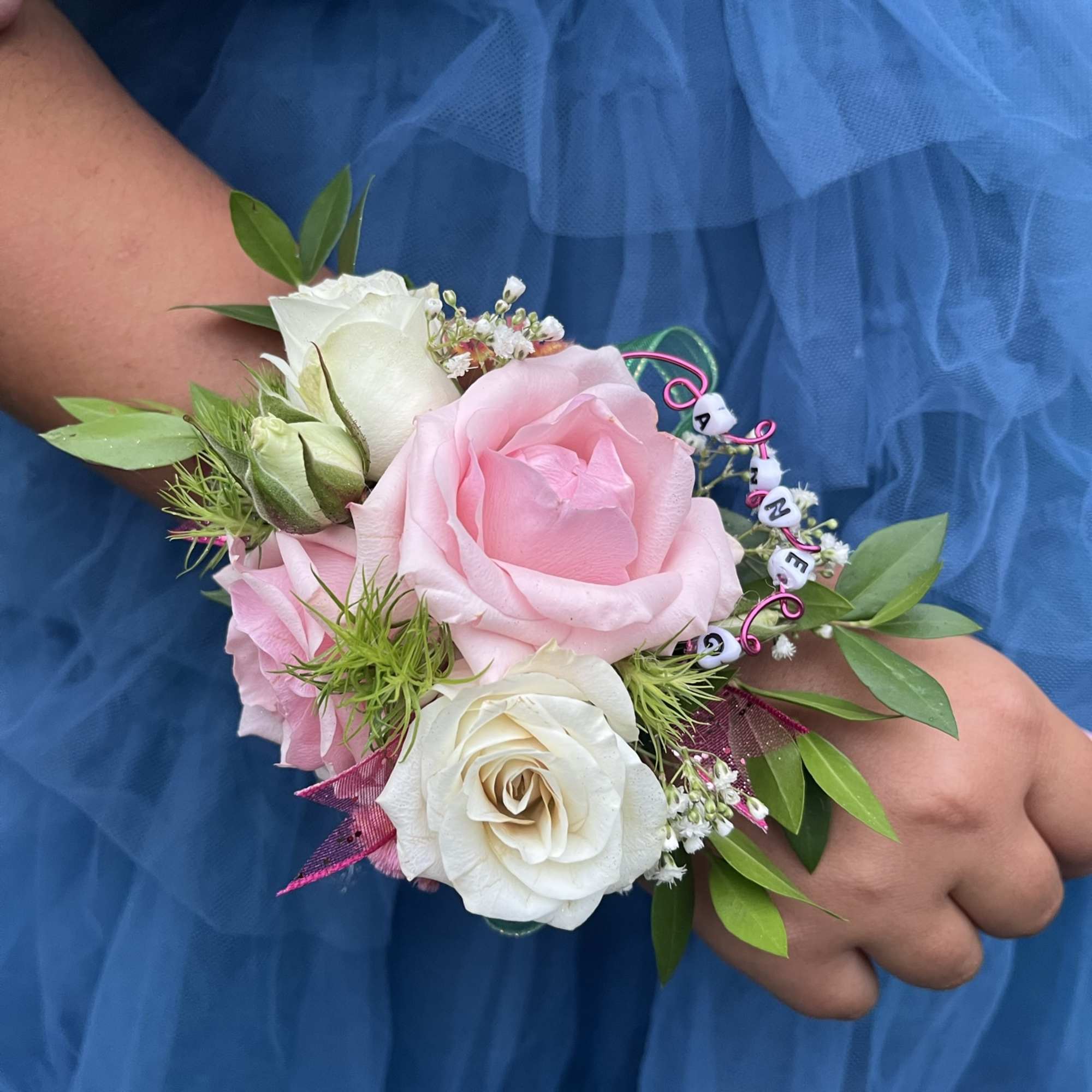 Pink and white rose wrist corsage with green accents on a blue dress
