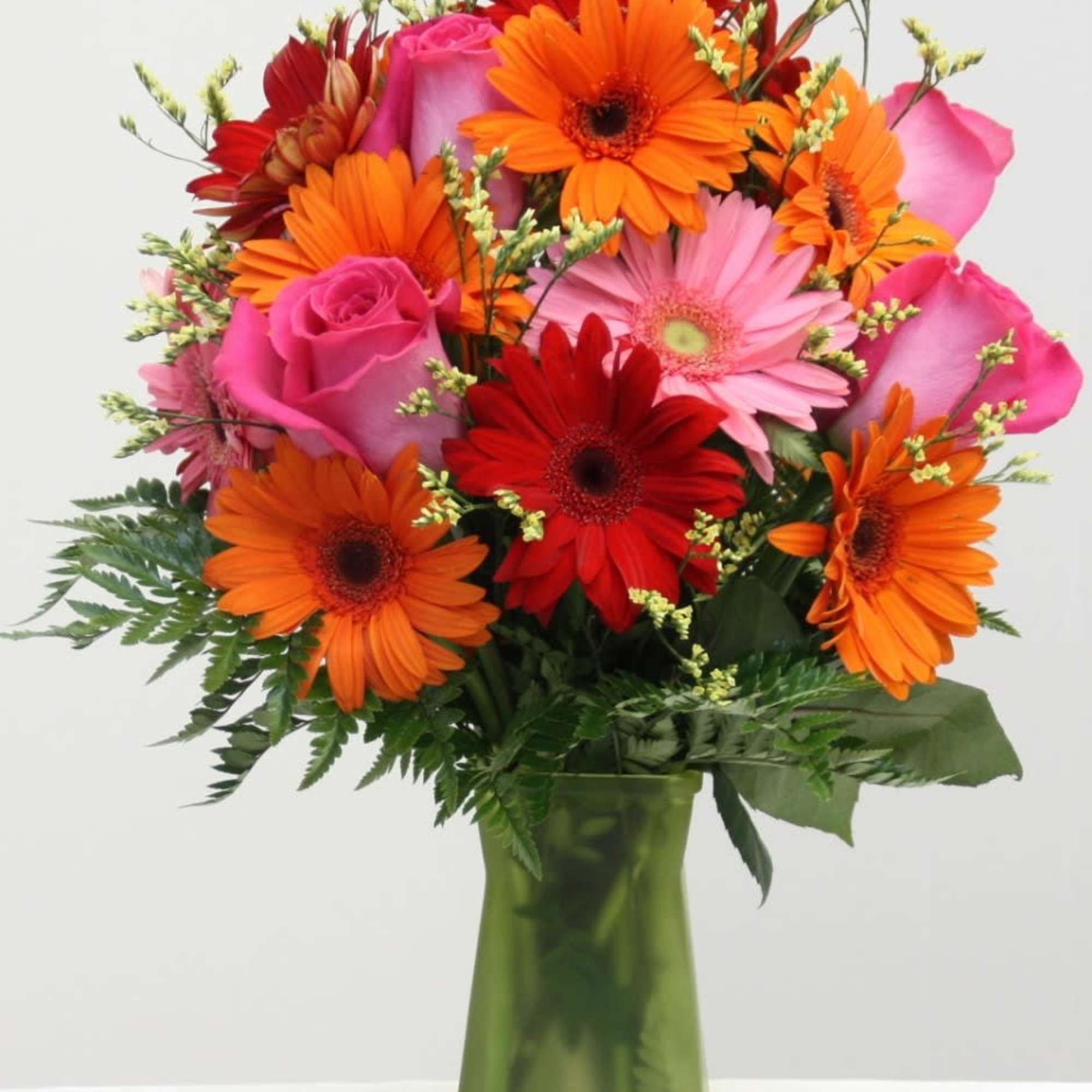 Bouquet of orange and pink gerbera daisies with roses in a green vase