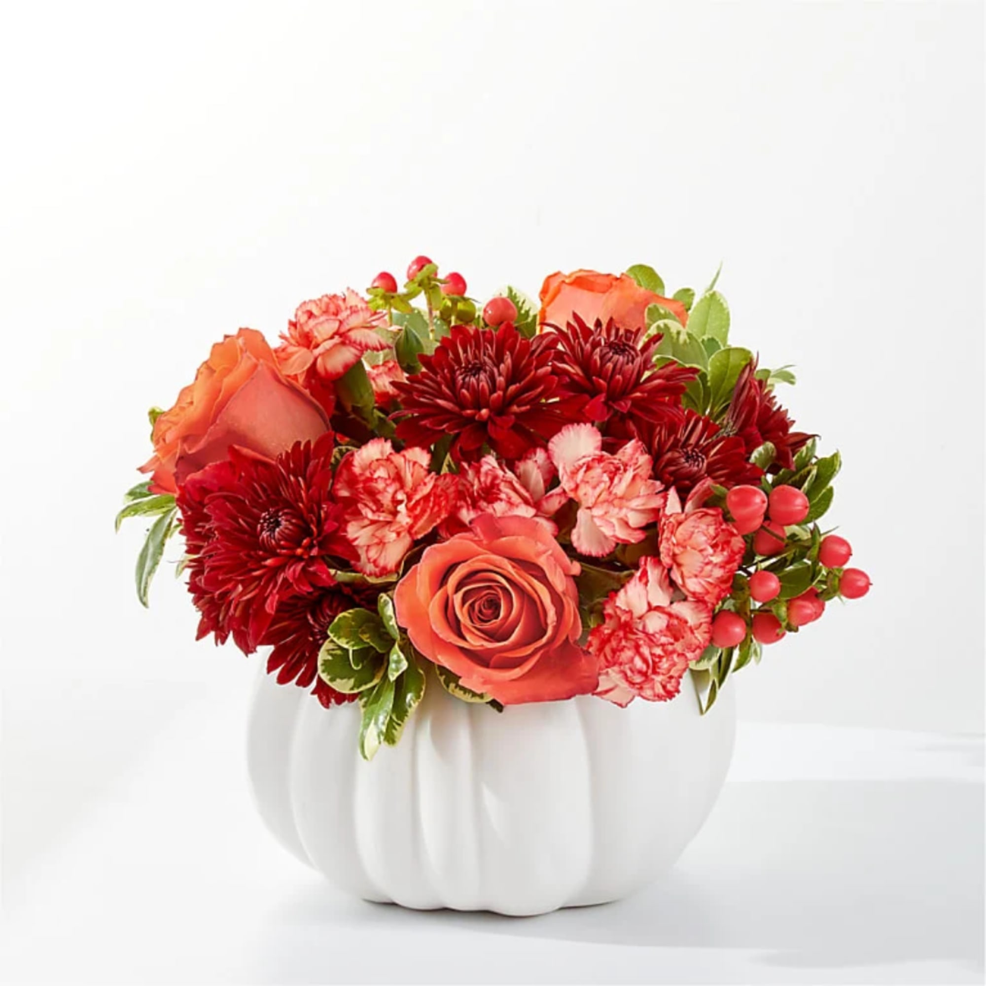 Orange and red floral arrangement in a white pumpkin vase