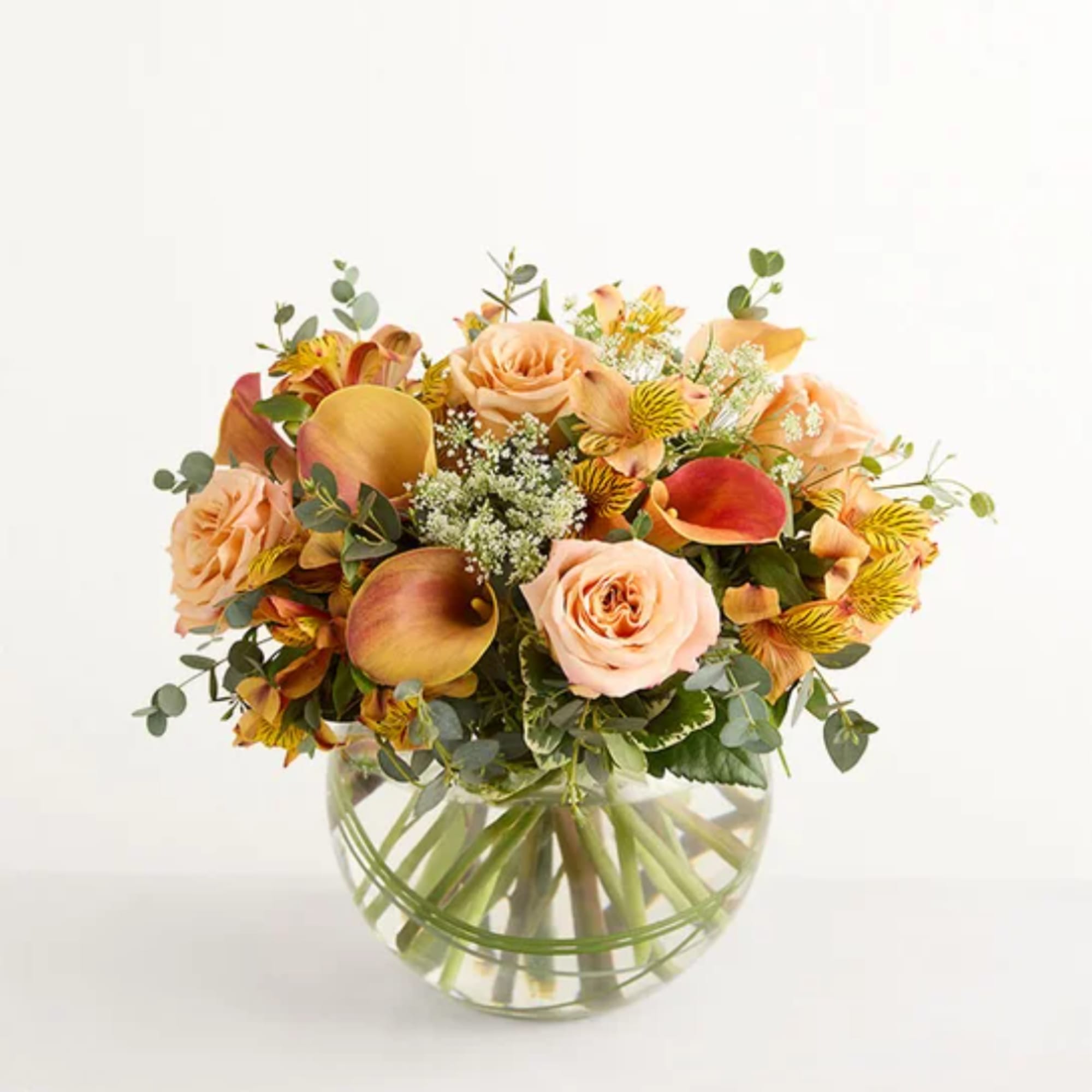 Peach and yellow flower bouquet in a round glass vase
