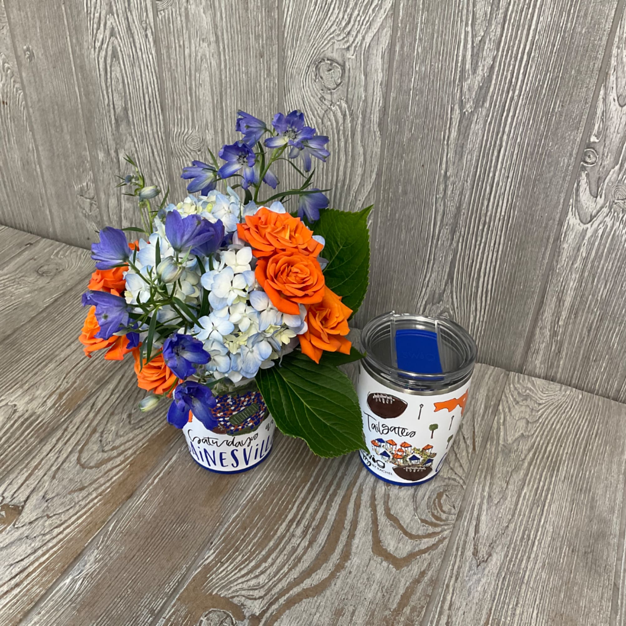 Orange roses and blue flowers arranged in a decorated tumbler vase