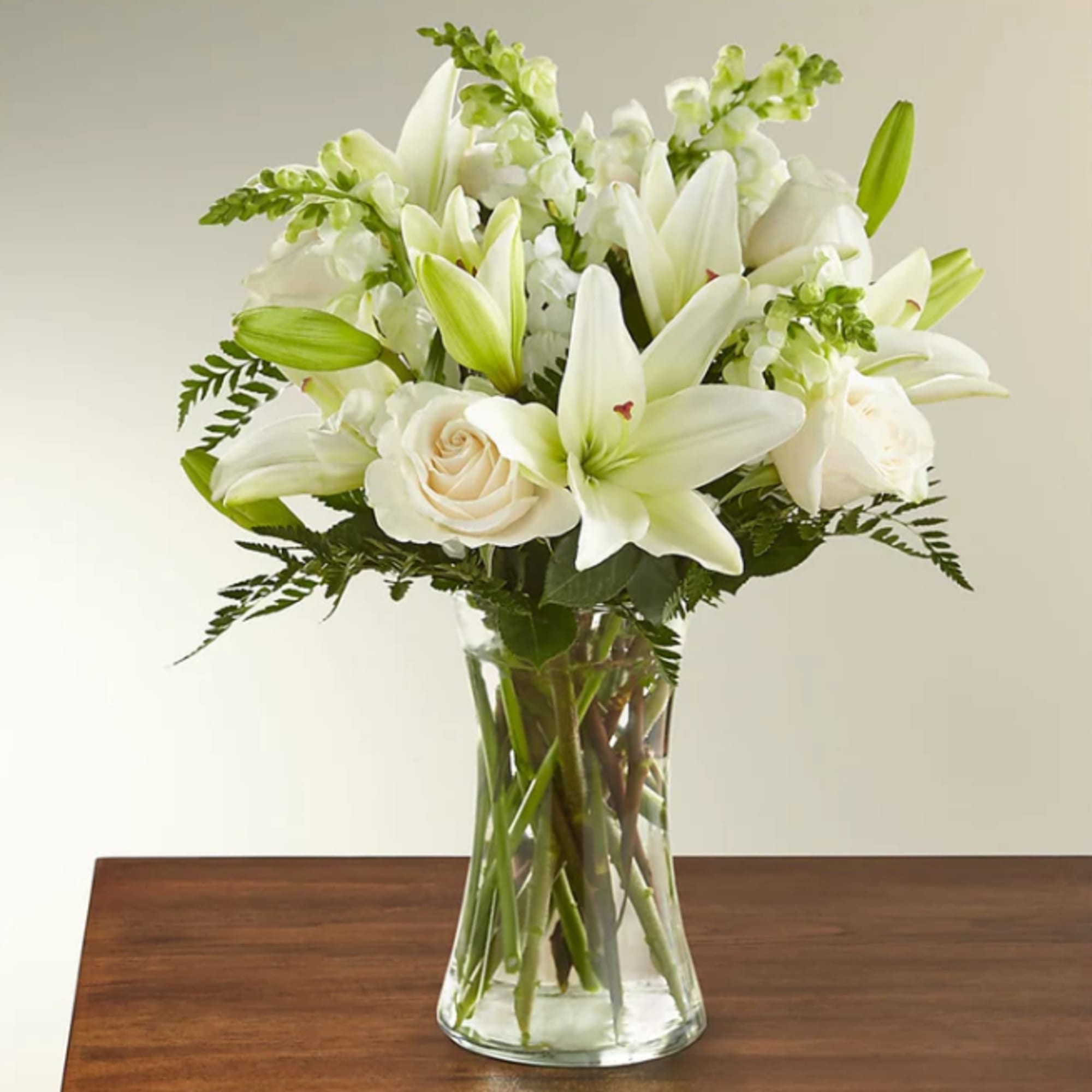 White lilies and roses arranged in a clear glass vase