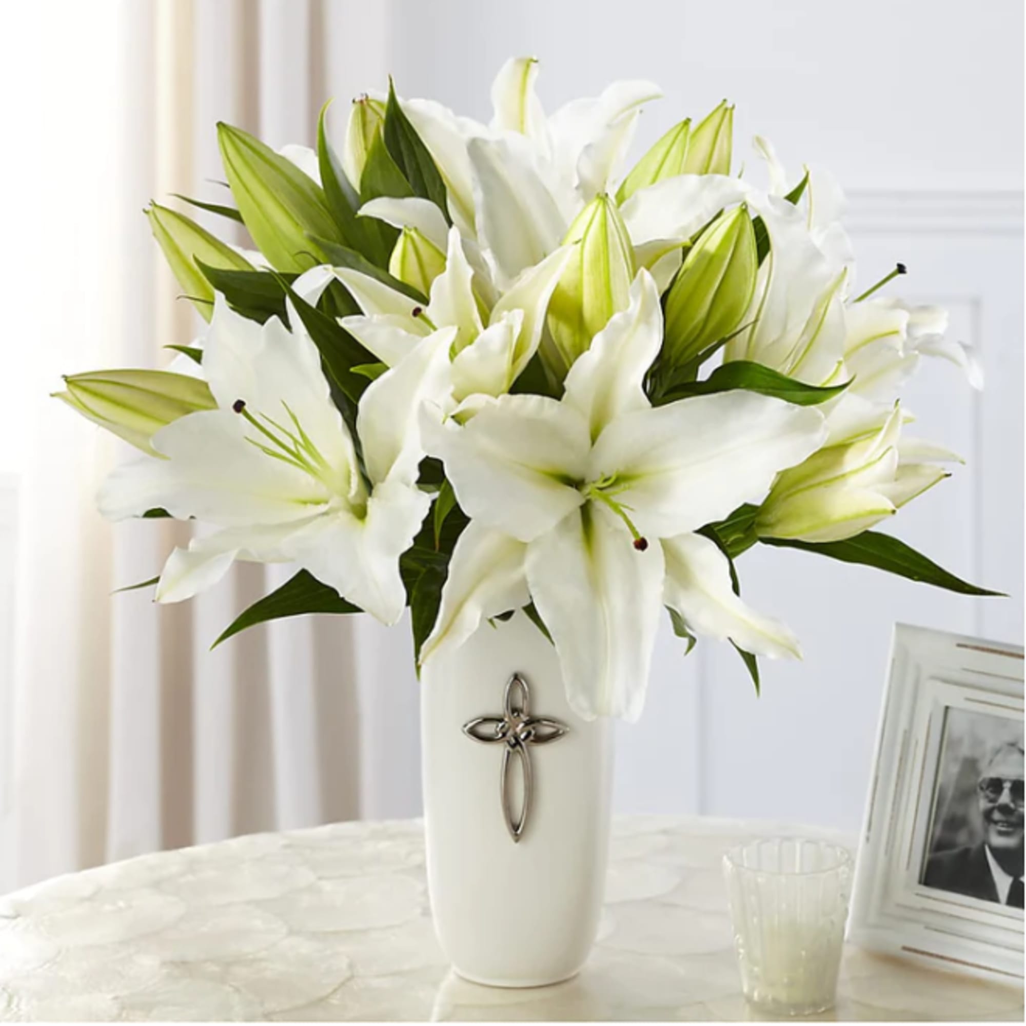 White lilies arranged in a white vase with a cross emblem