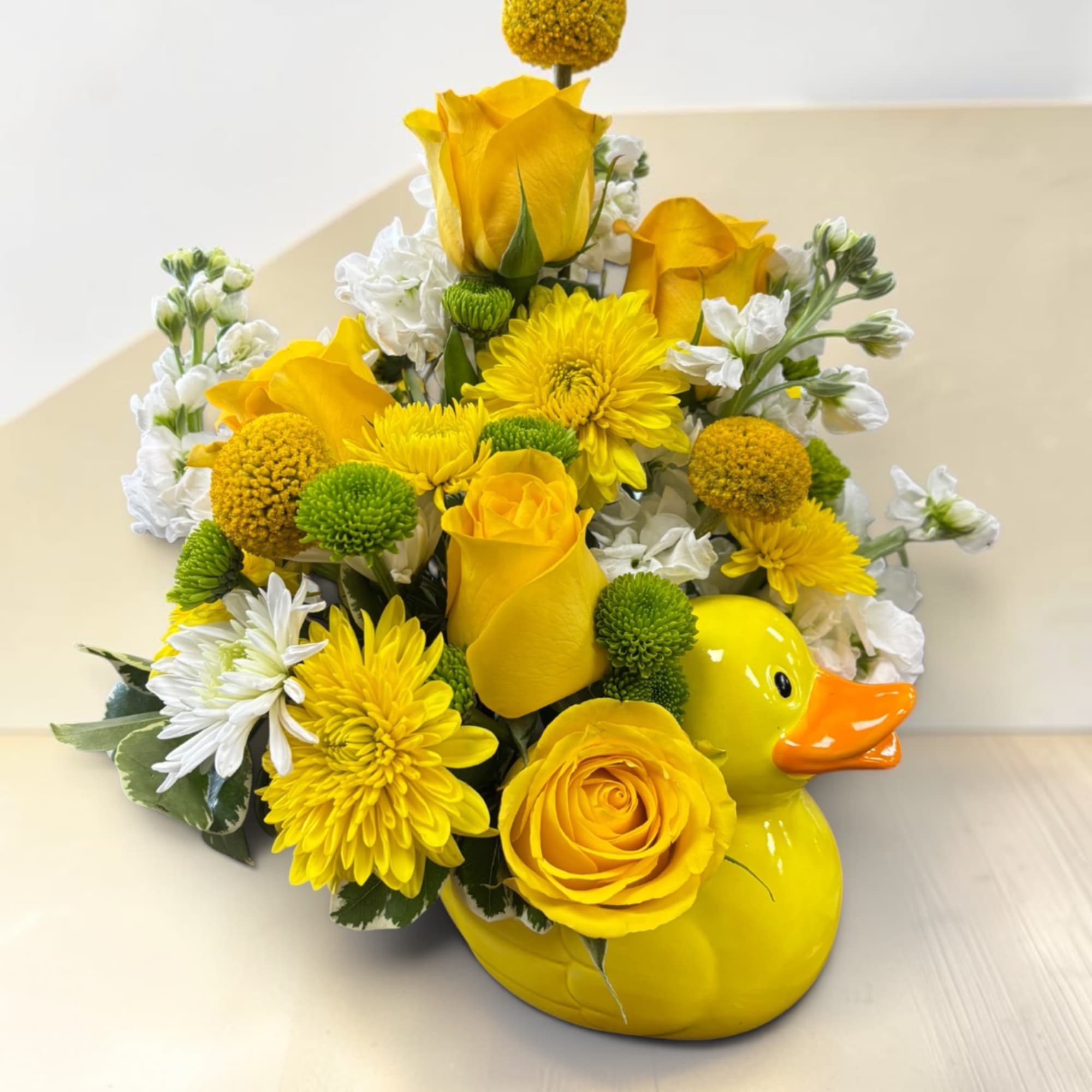 Yellow floral arrangement in a duck-shaped vase with white accents