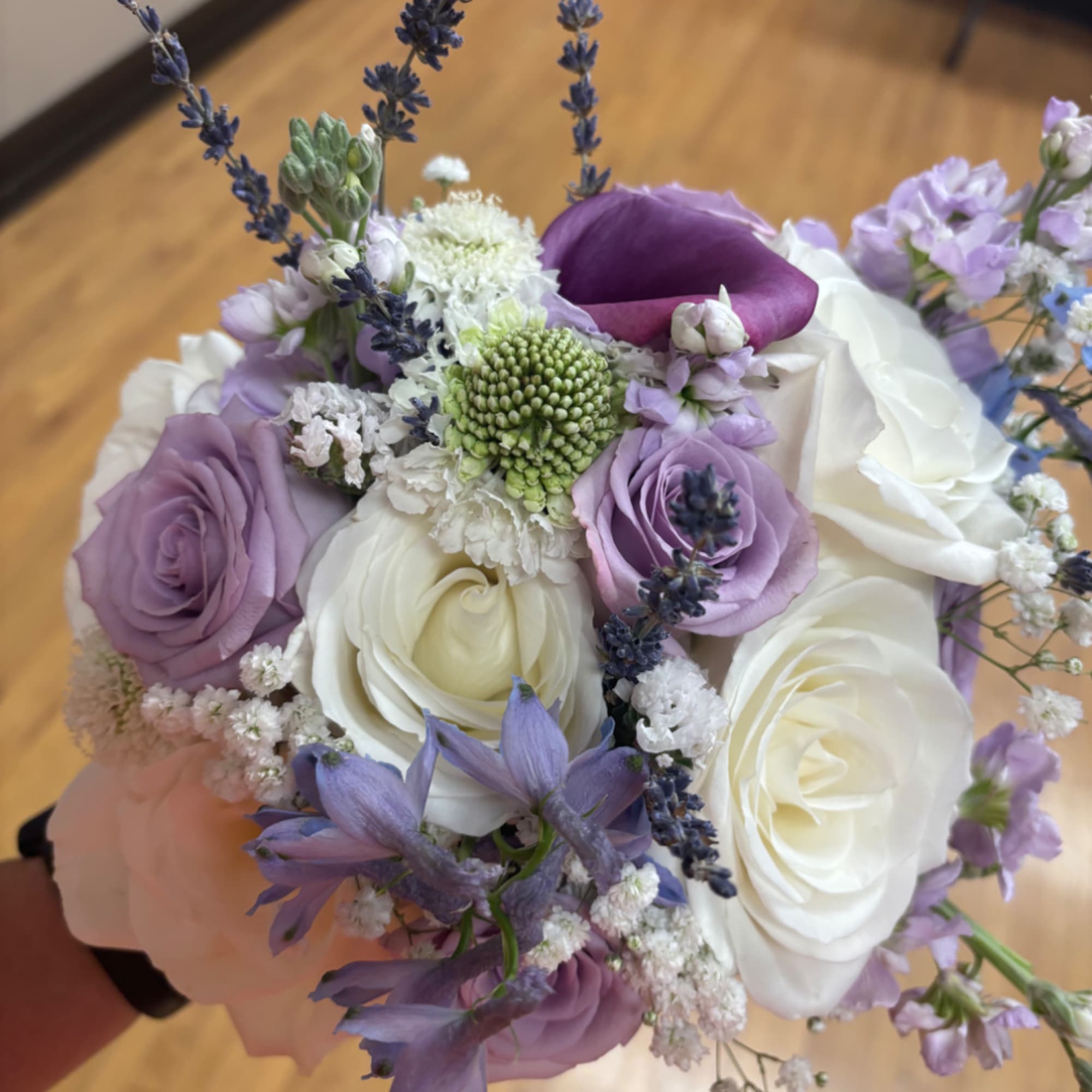 Handheld bouquet of white and lavender roses with purple accent flowers