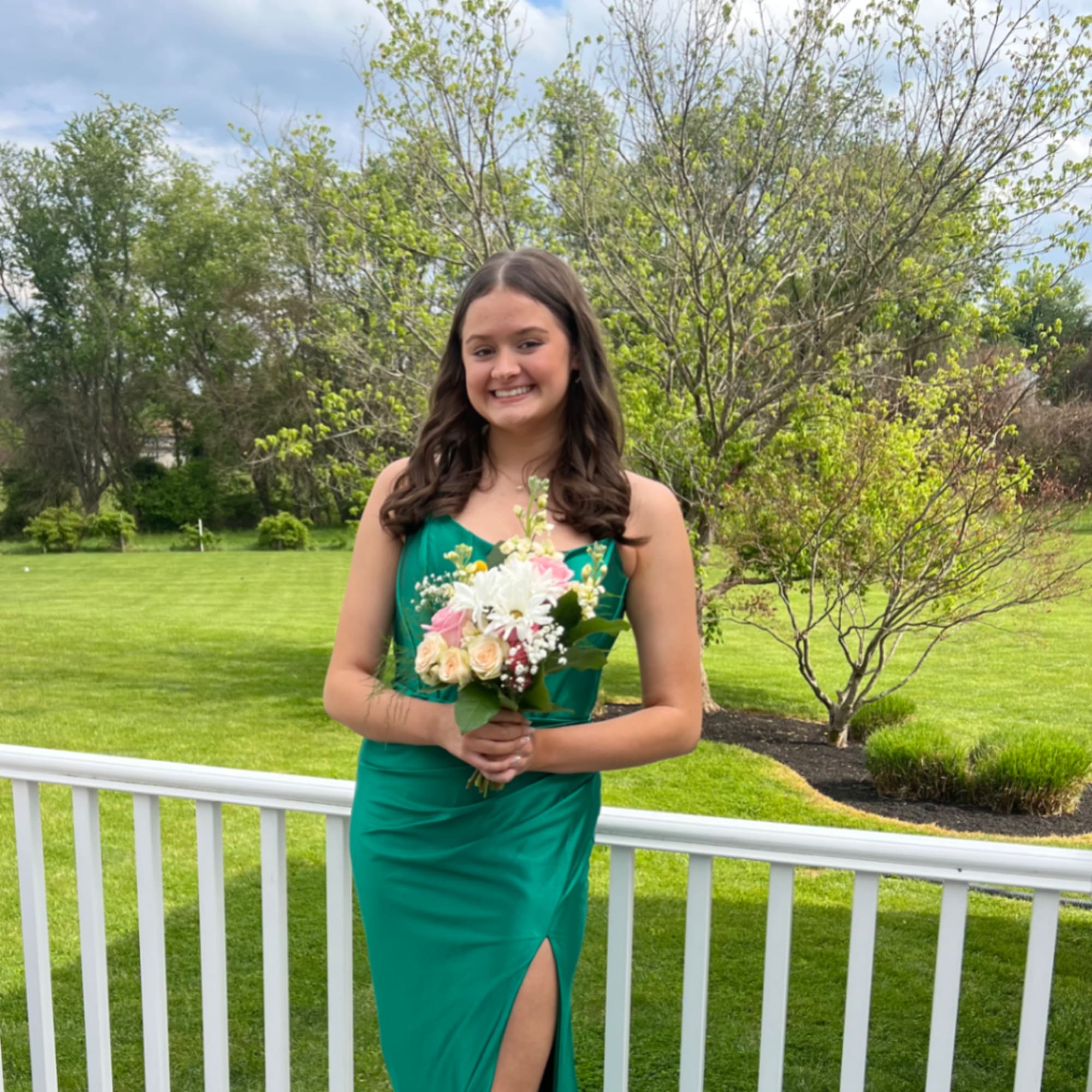 Young woman in a green dress holding a small bouquet outdoors