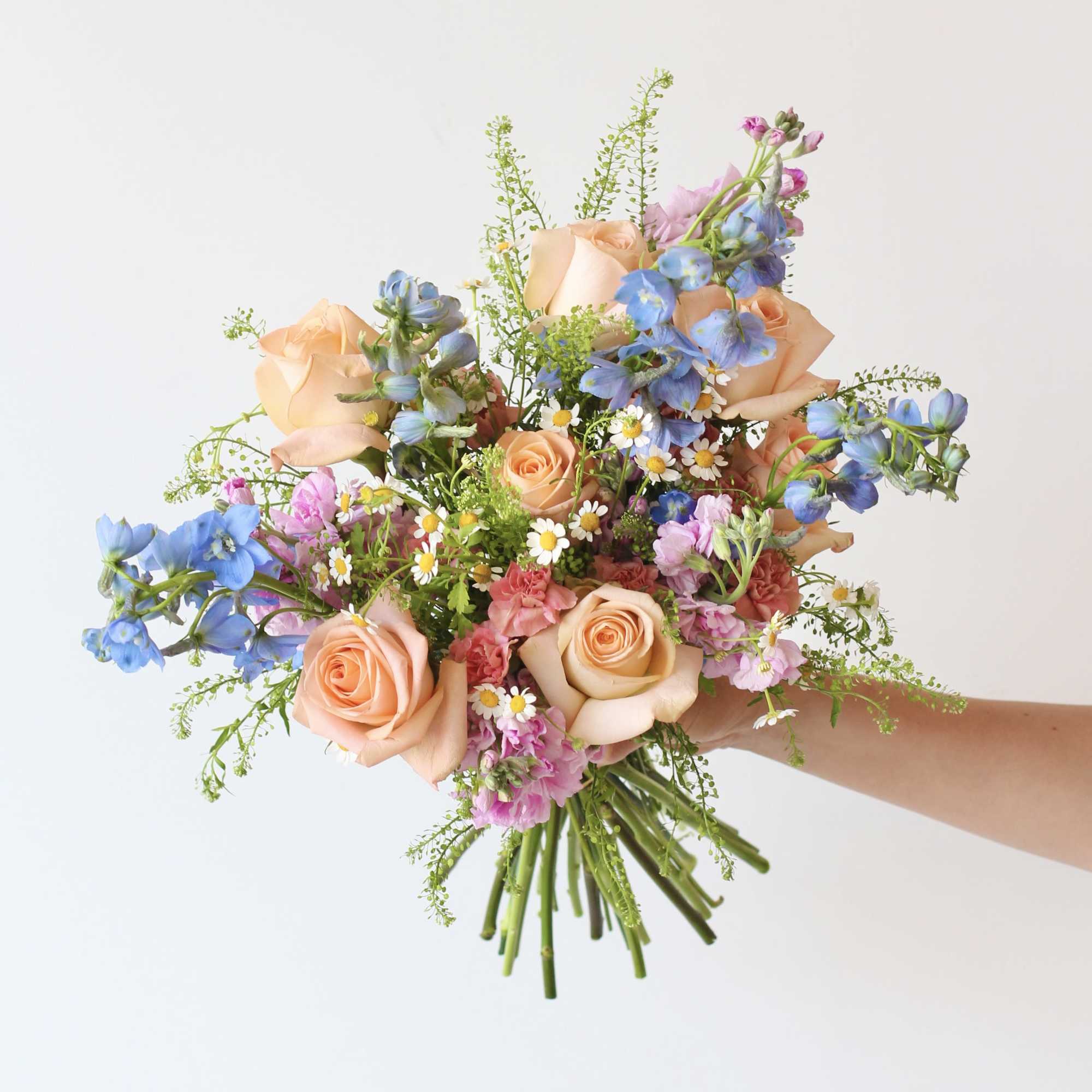 Handheld bouquet of peach roses, blue flowers, and pink accents