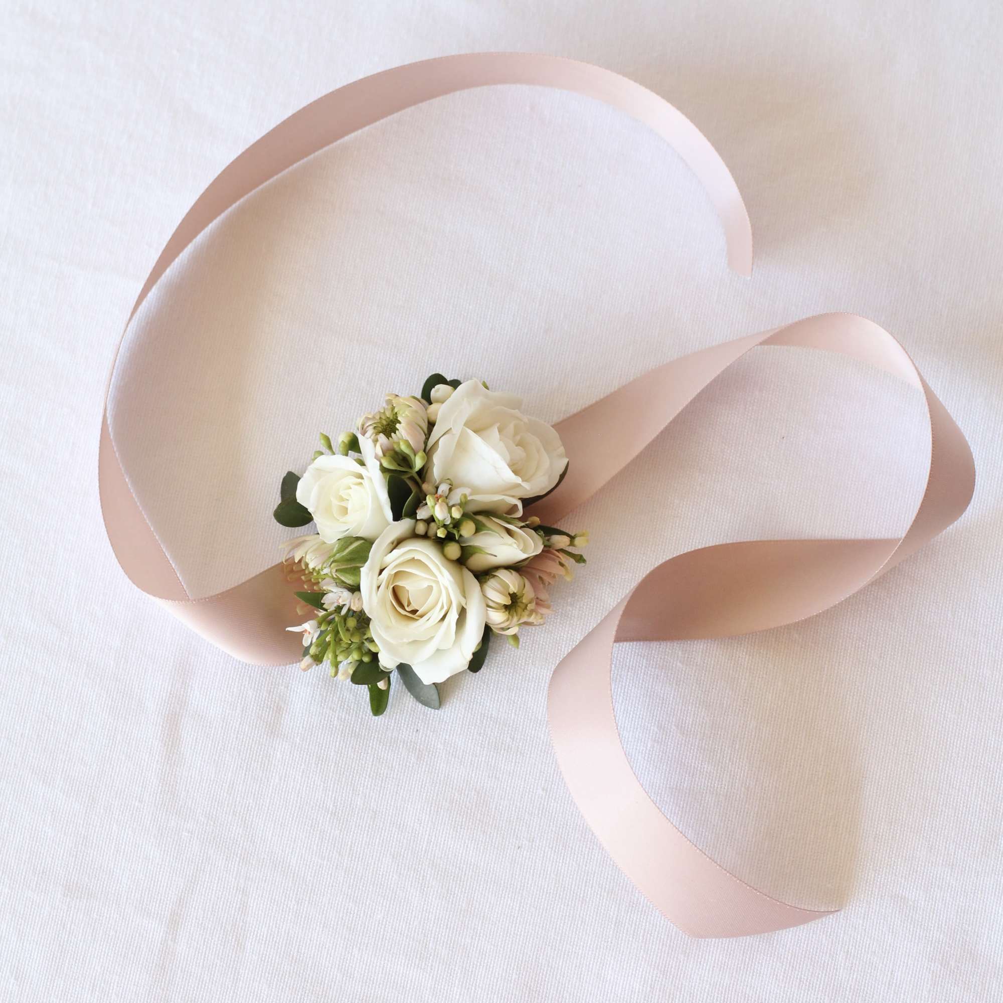 Small white rose corsage with pale pink ribbon on white fabric