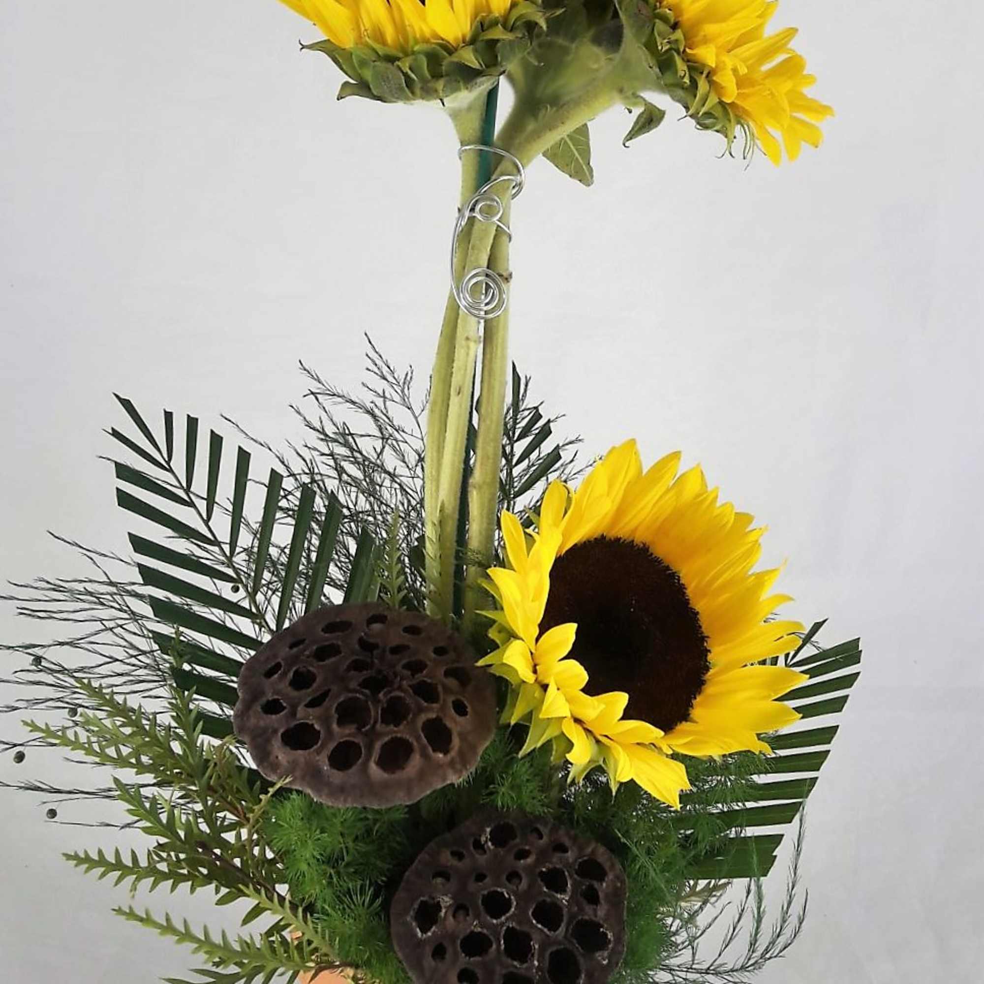 Sunflower arrangement with lotus pods and greenery in a vase