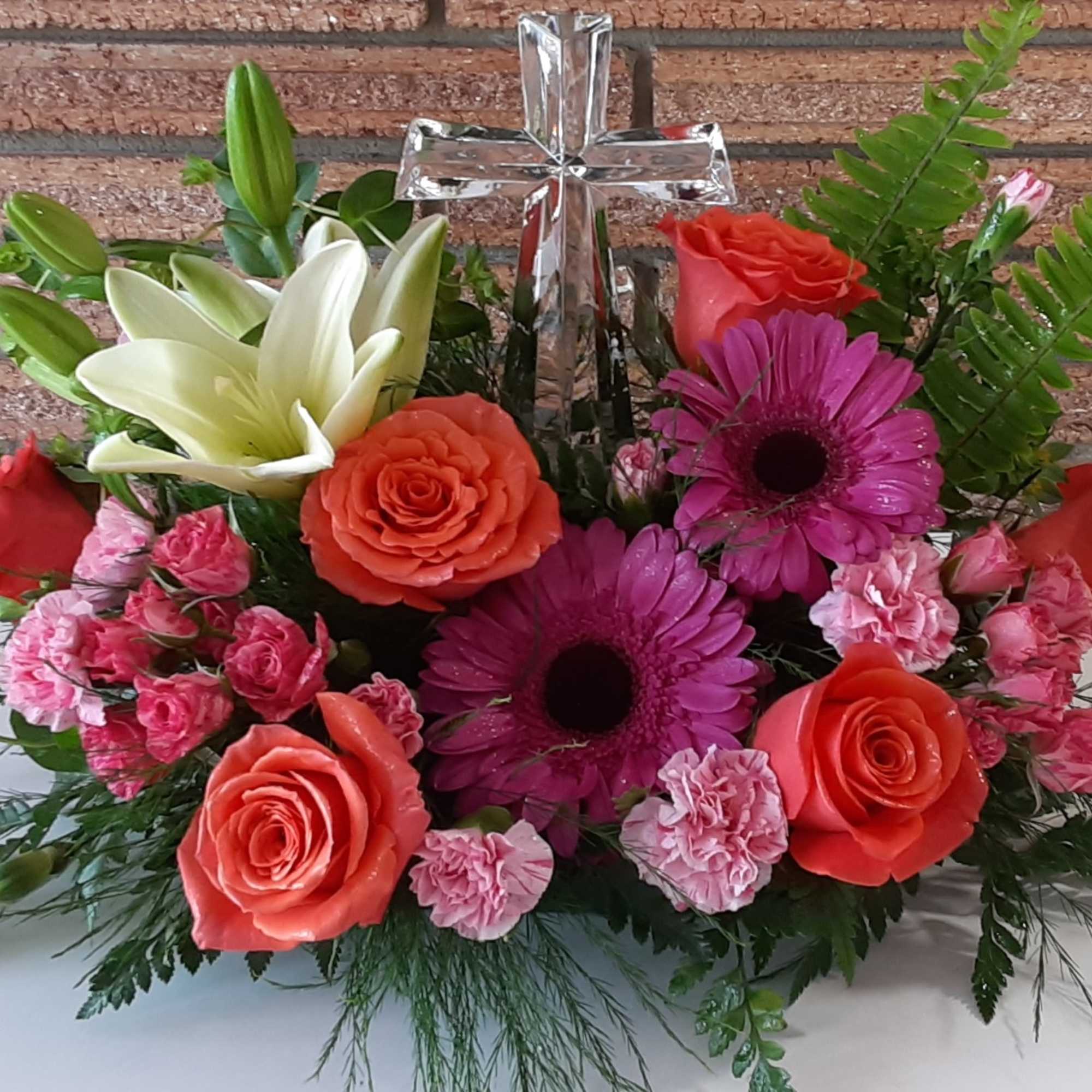 Mixed bouquet with roses, gerbera daisies, lilies, and carnations around a clear cross