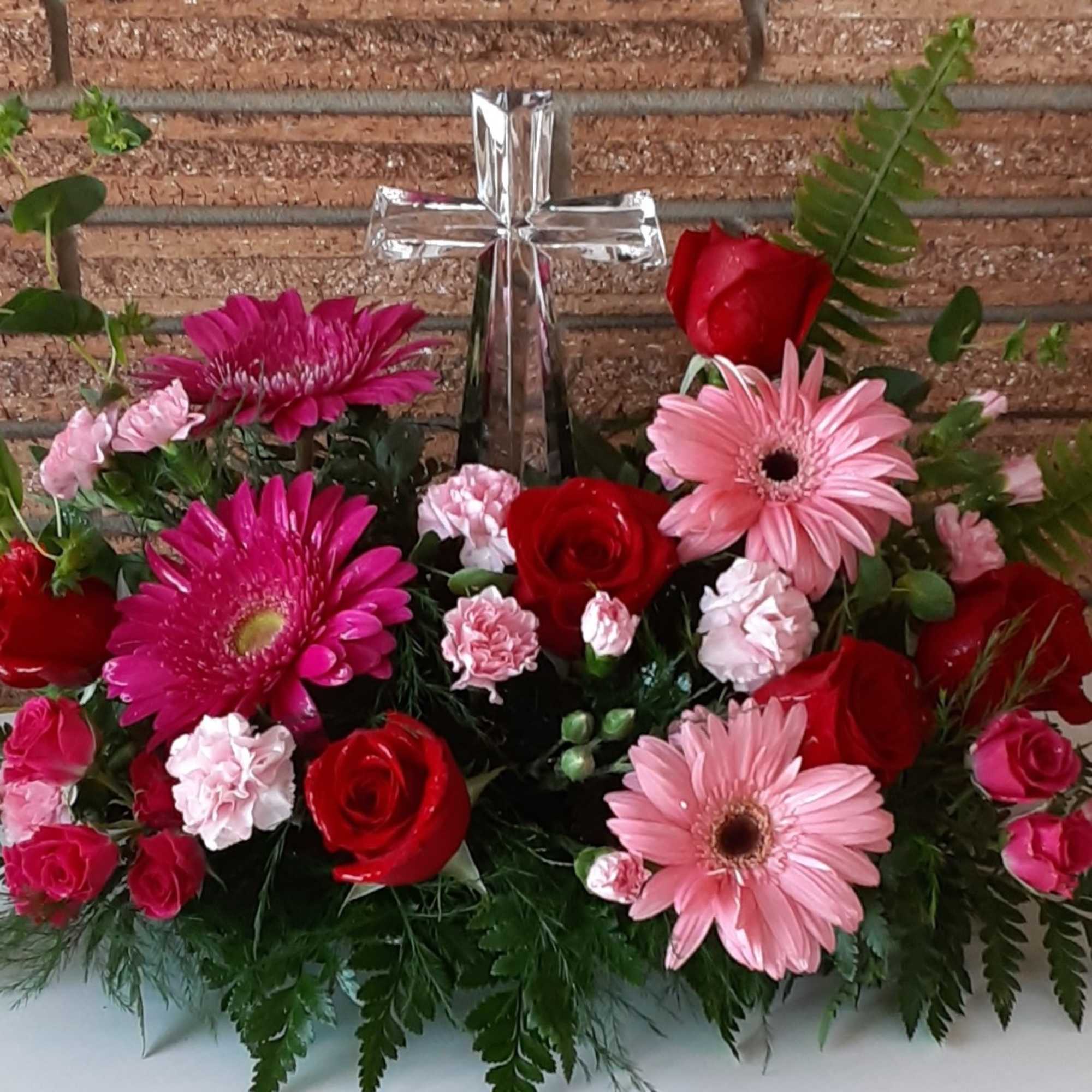 Floral arrangement with red and pink flowers around a silver cross