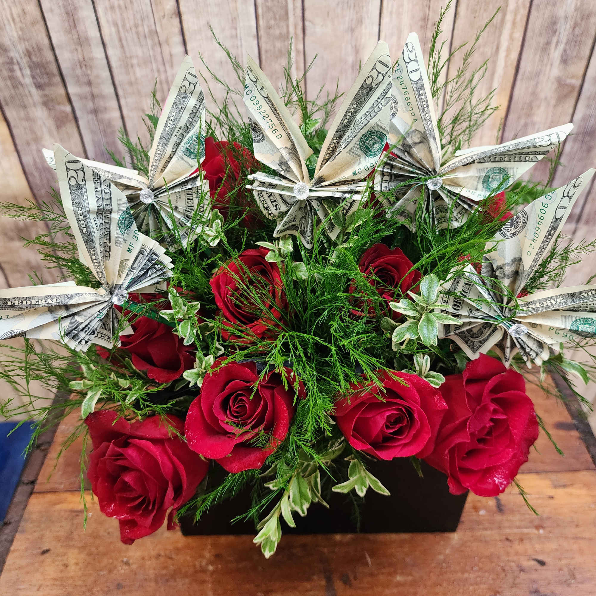 Red roses arranged with folded dollar bills in a black container