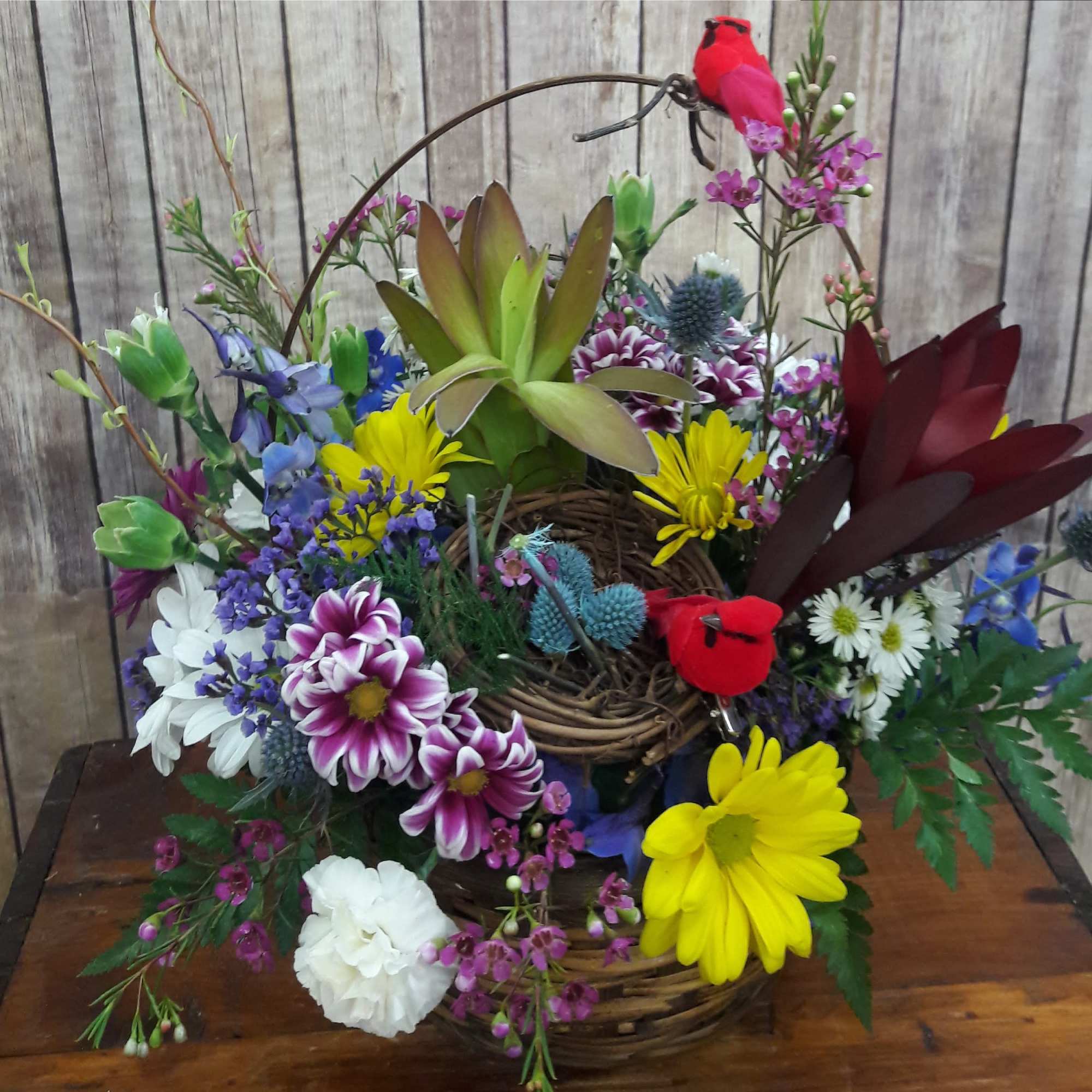Colorful mixed flower arrangement in a woven basket with a bird decoration
