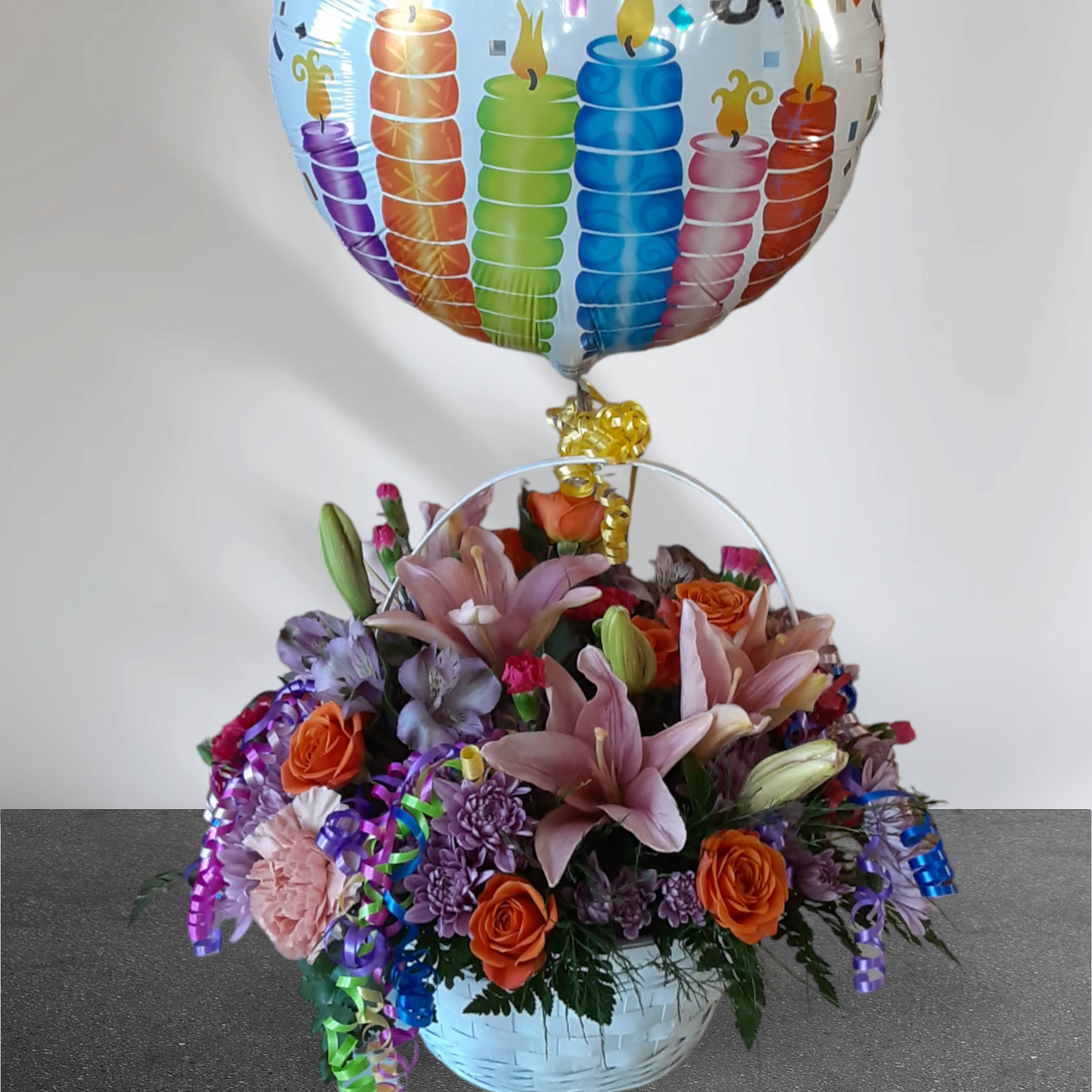 Basket of mixed flowers with a colorful candle balloon above it