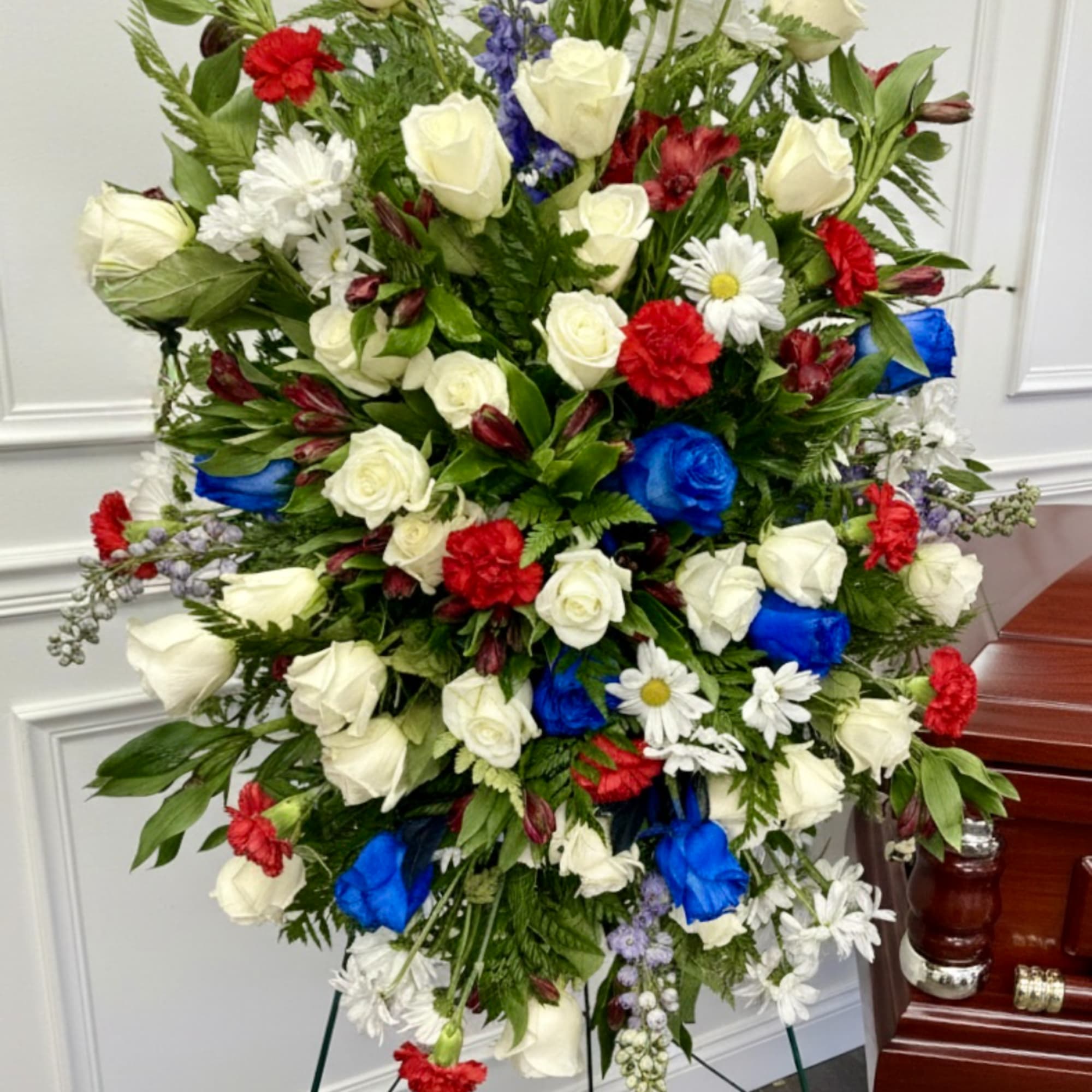 Large standing floral spray with white roses, red carnations, blue roses, and daisies