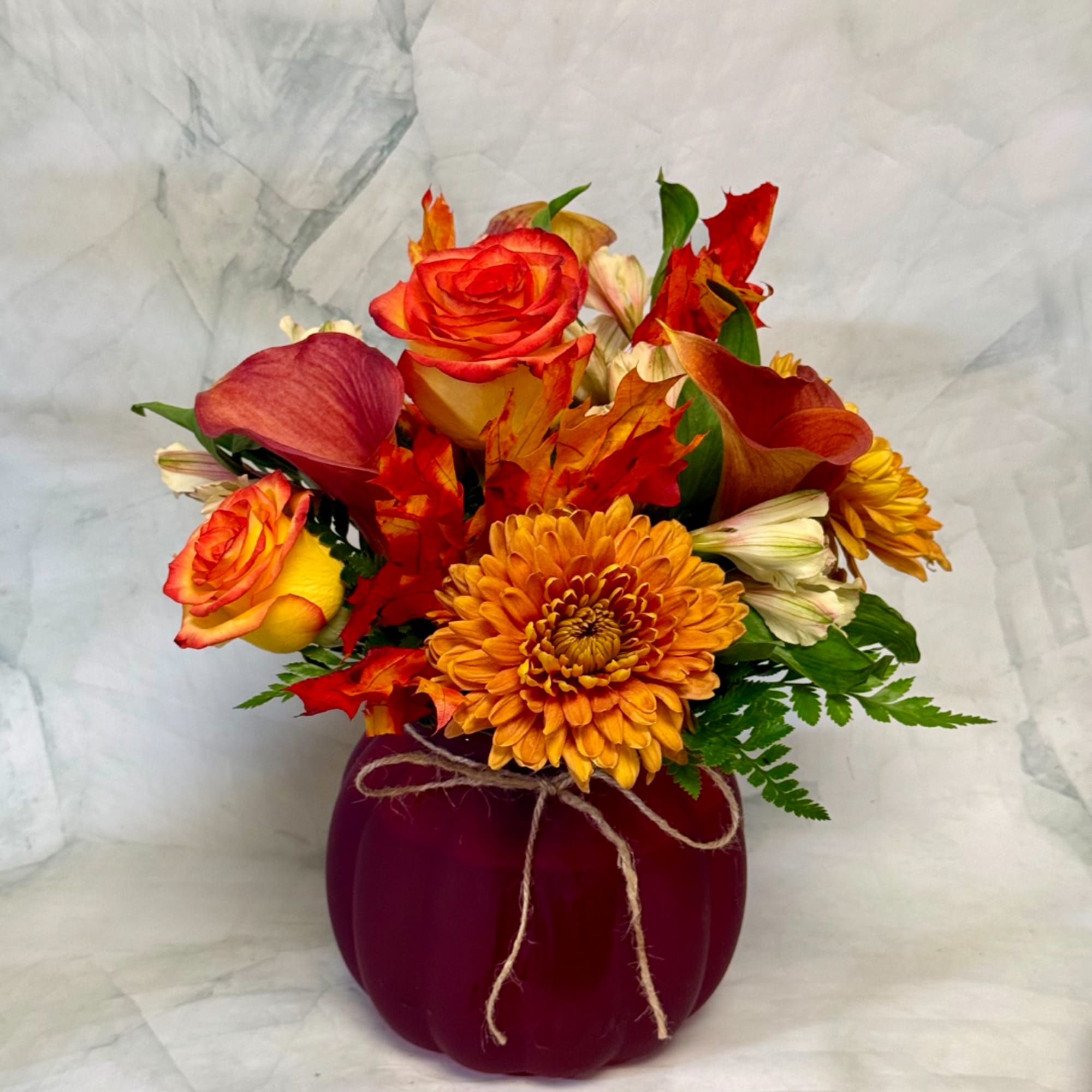 Autumn bouquet with orange roses, calla lilies, and chrysanthemums in a purple pumpkin vase
