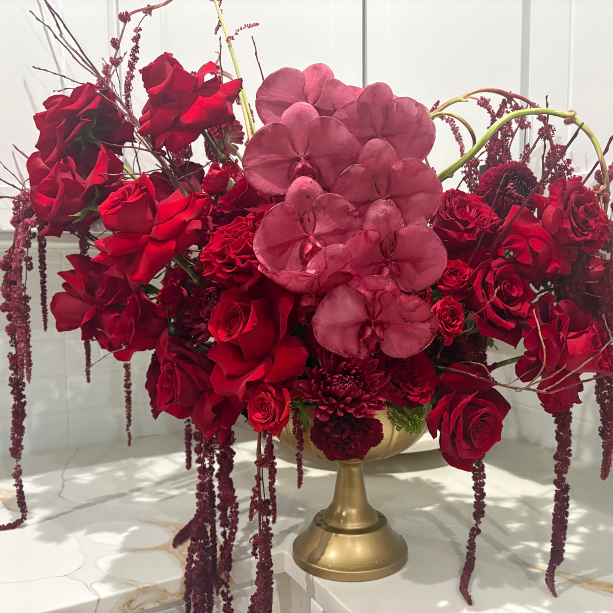Red rose arrangement with pink orchid blooms in a gold pedestal vase