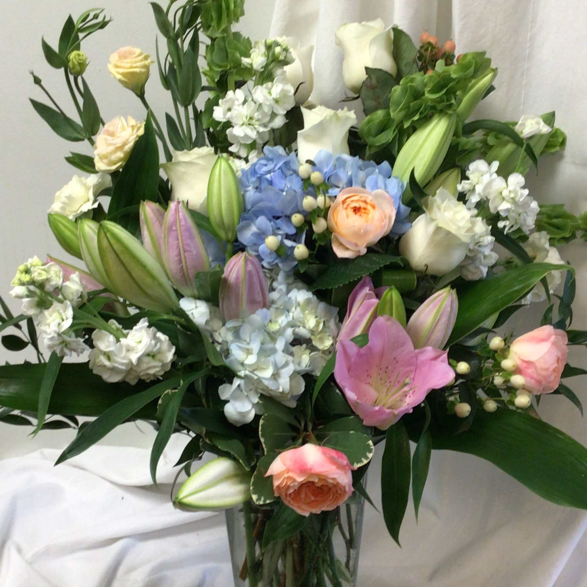 Mixed bouquet of lilies, roses, hydrangeas, and white blooms in a glass vase