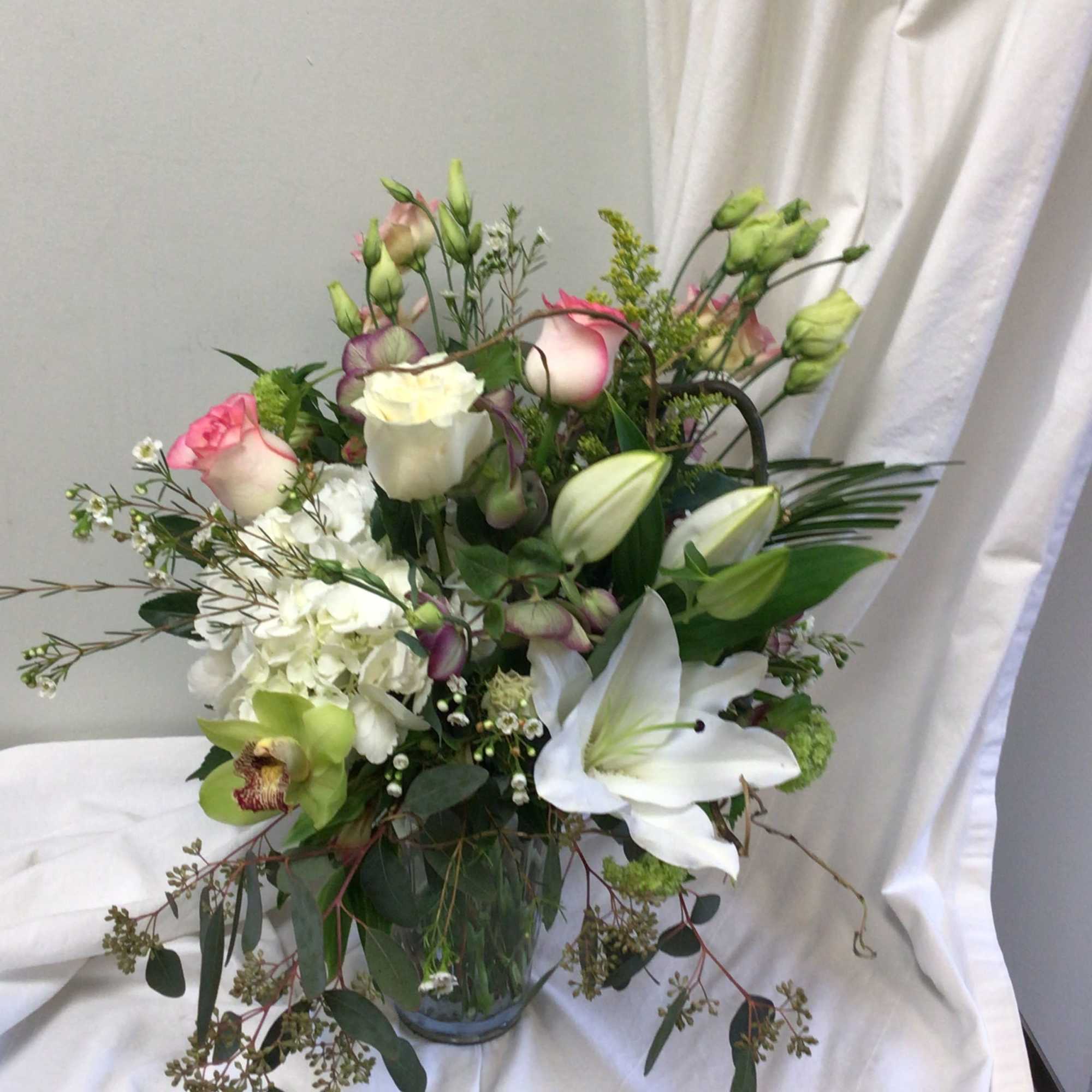 Mixed bouquet with white lilies, roses, and green blooms in a glass vase