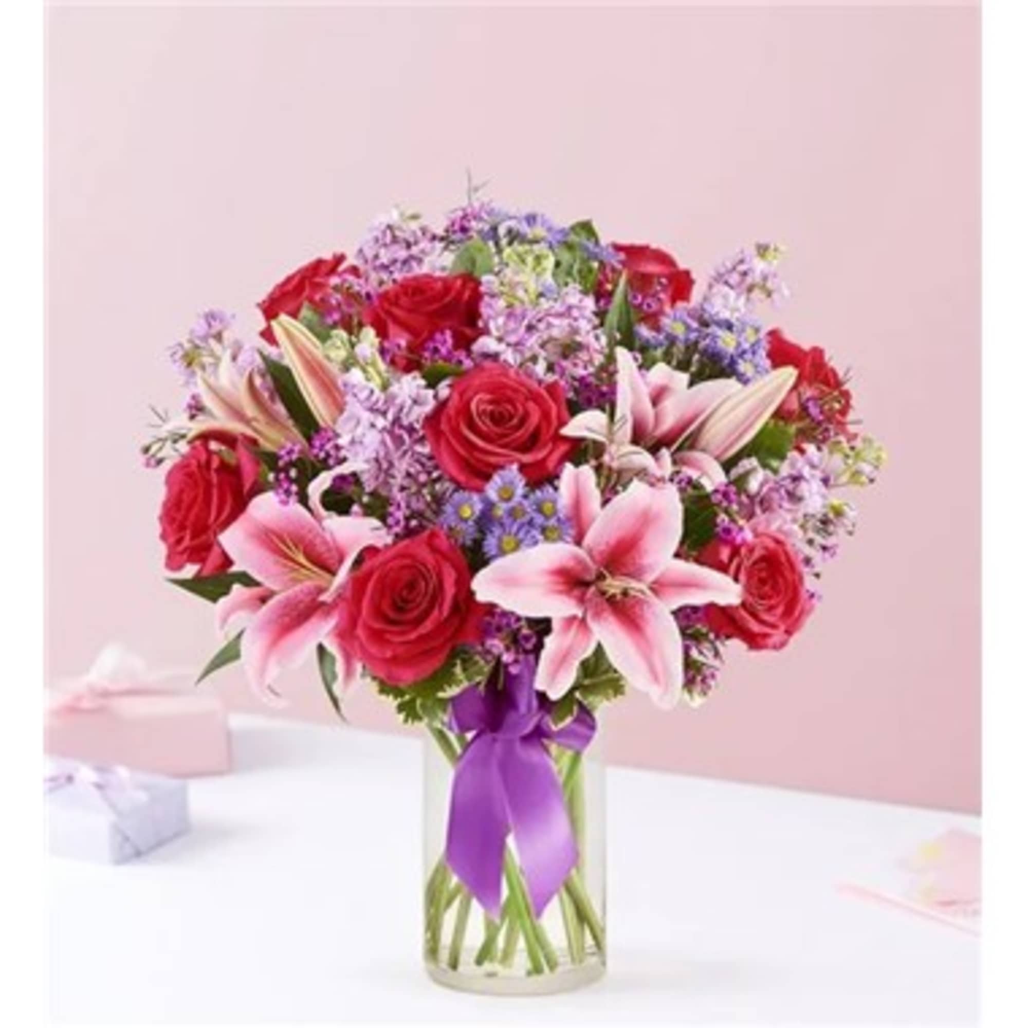 Bouquet of pink lilies and red roses in a glass vase with a purple ribbon