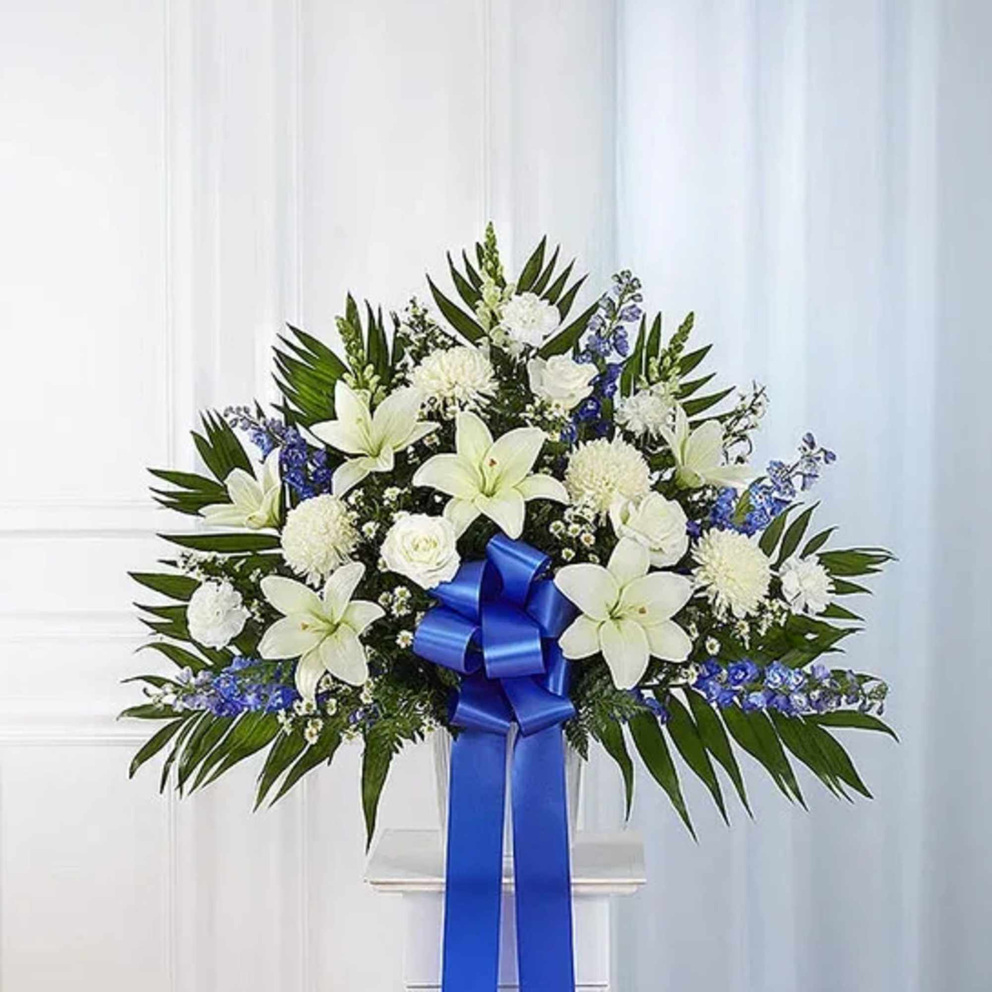White lilies and blue flowers in a standing arrangement with a blue ribbon