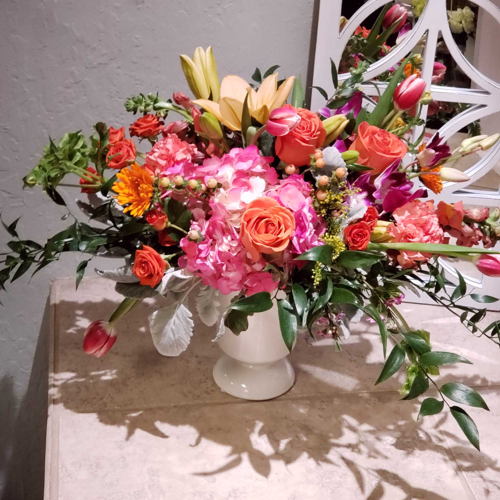 Mixed bouquet in a white pedestal vase with pink, orange, and yellow blooms