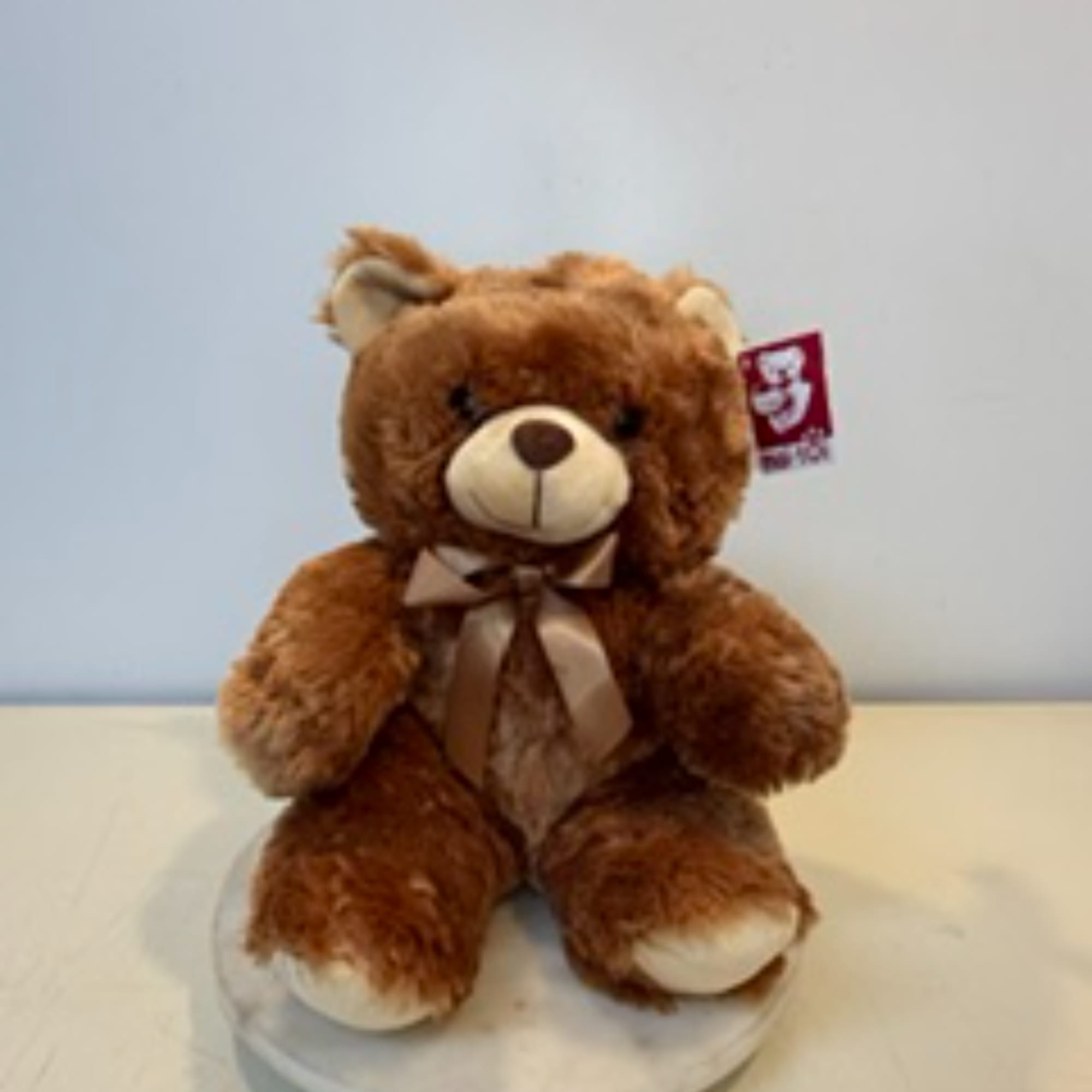 Brown teddy bear with a ribbon bow sitting on a round base