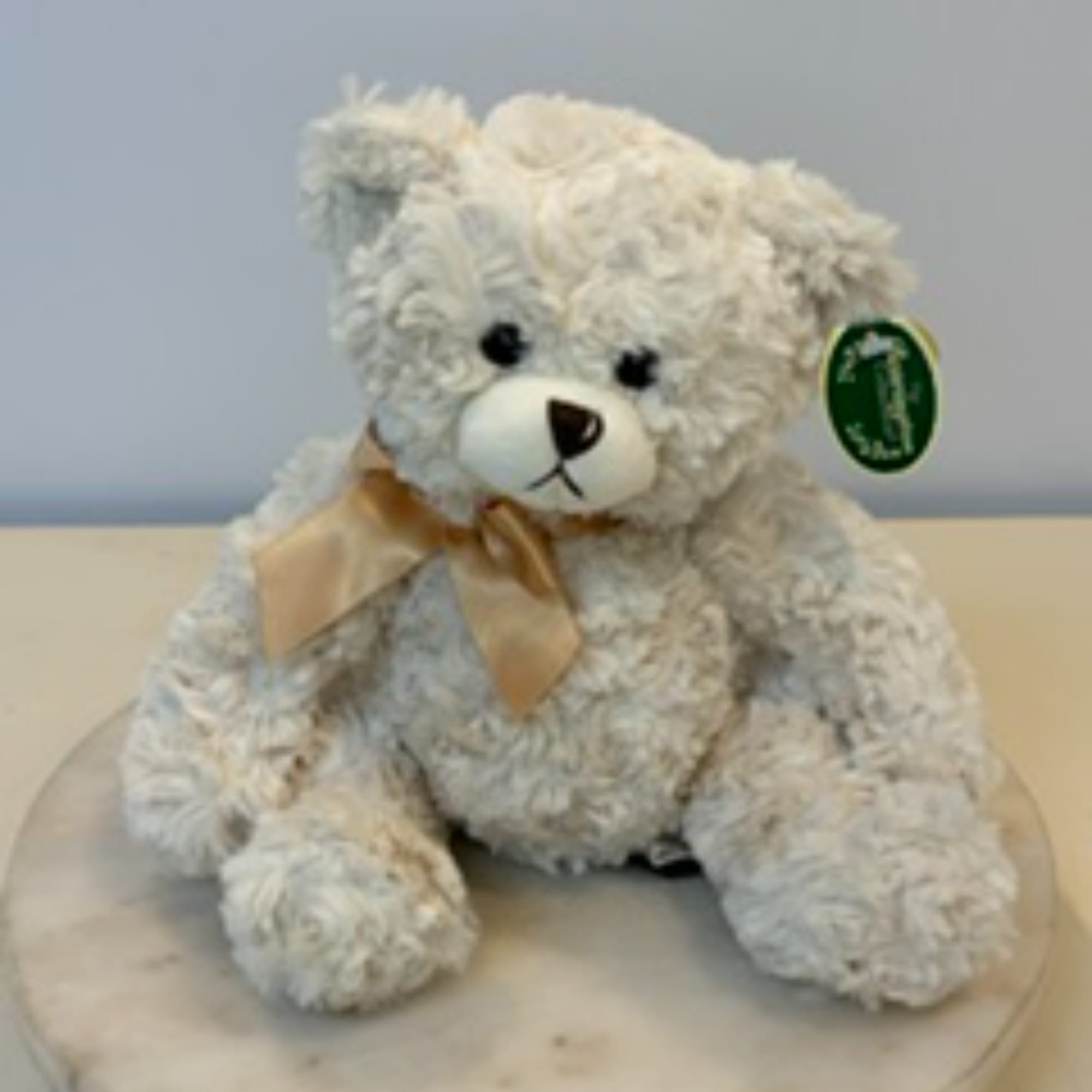 White teddy bear with a satin bow sitting on a round surface