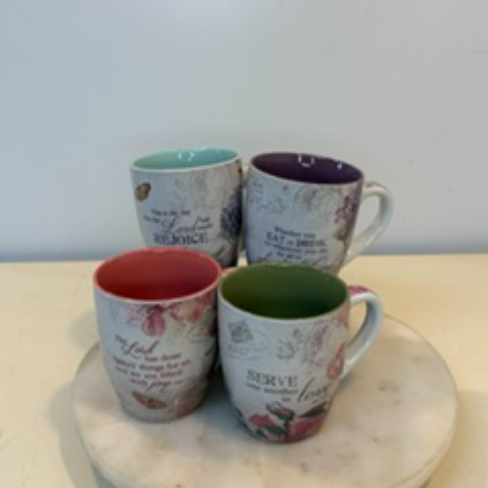 Four floral quote mugs with colored interiors arranged on a round tray