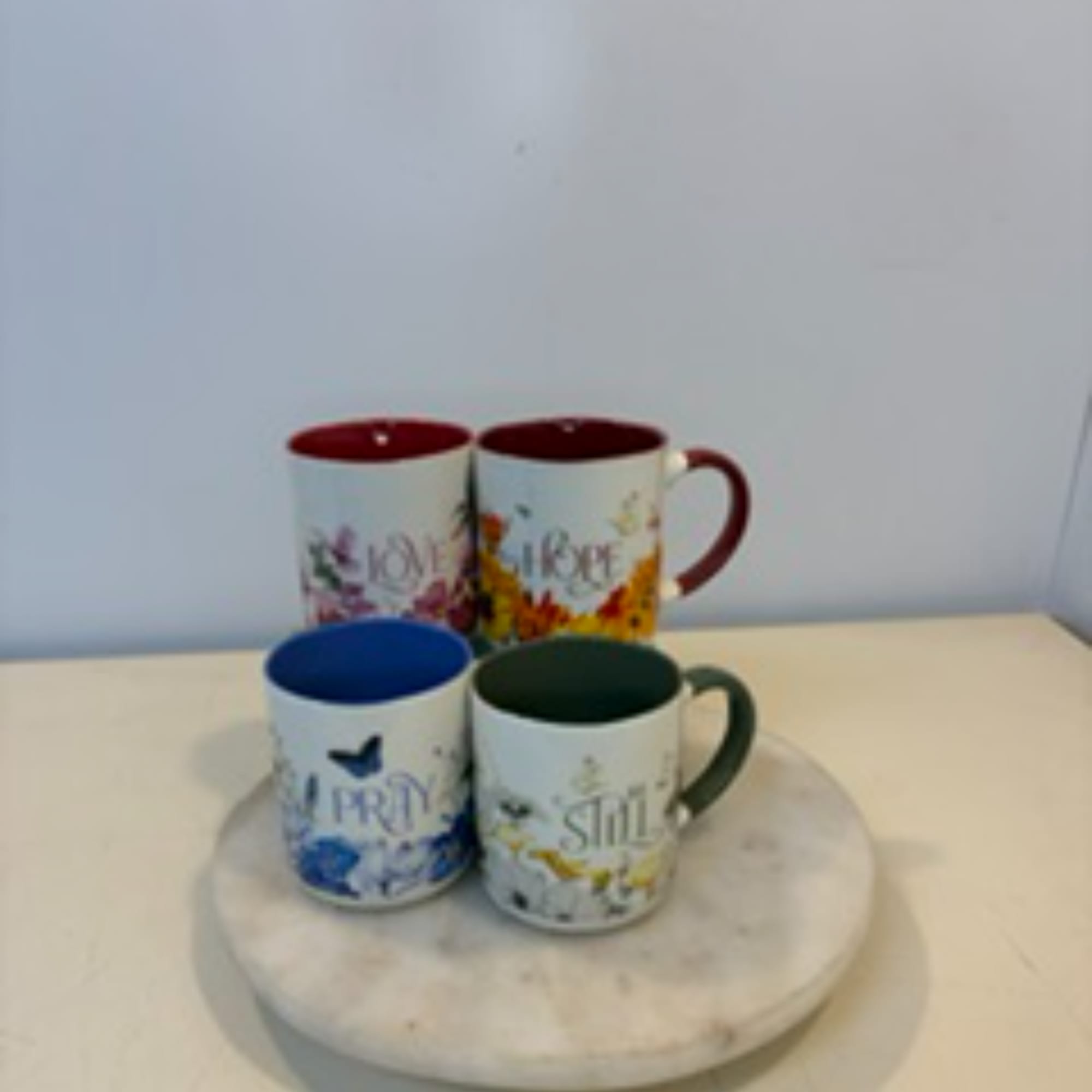 Four floral-themed mugs arranged on a round marble tray