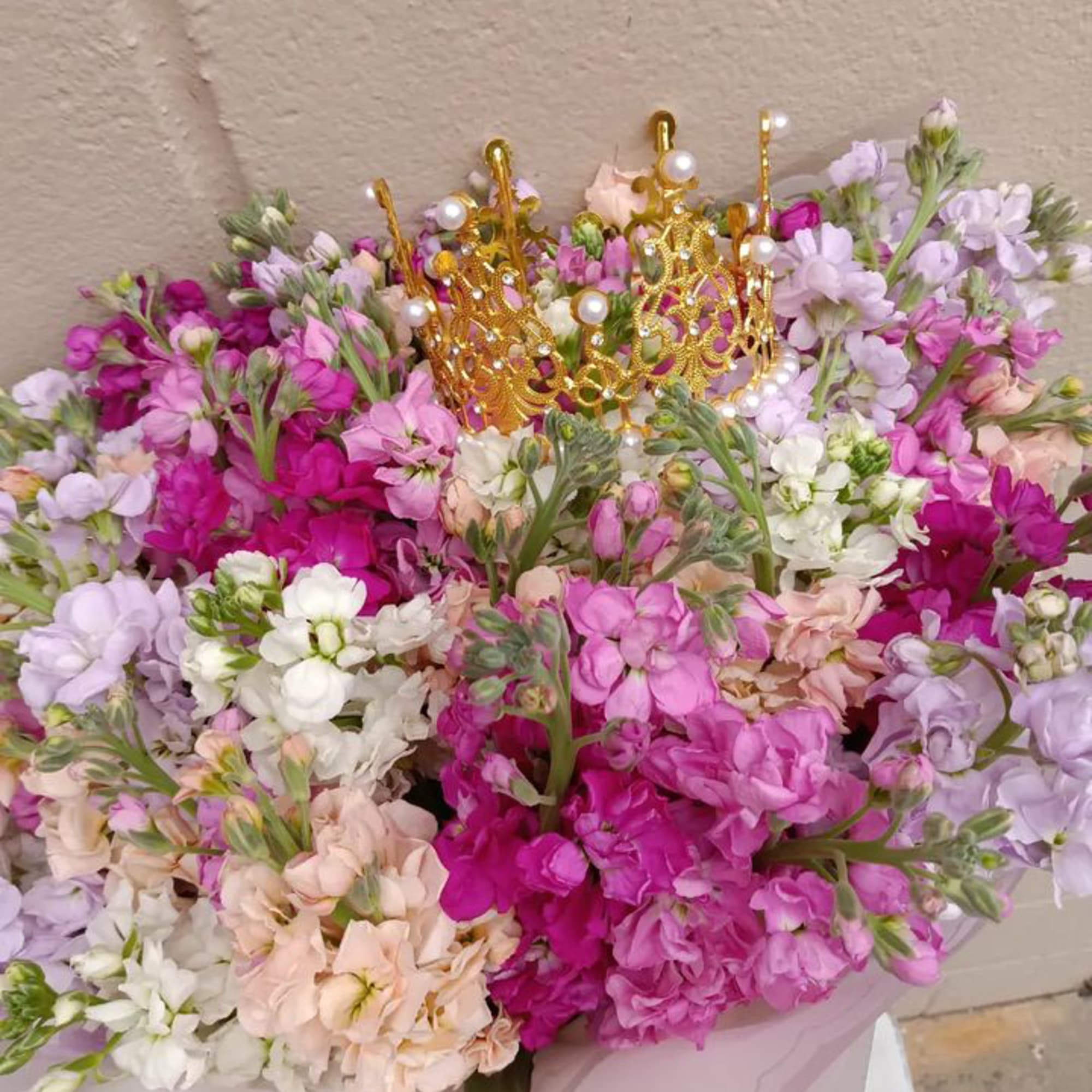 Large bouquet of pink, lavender, and white flowers with gold crown toppers
