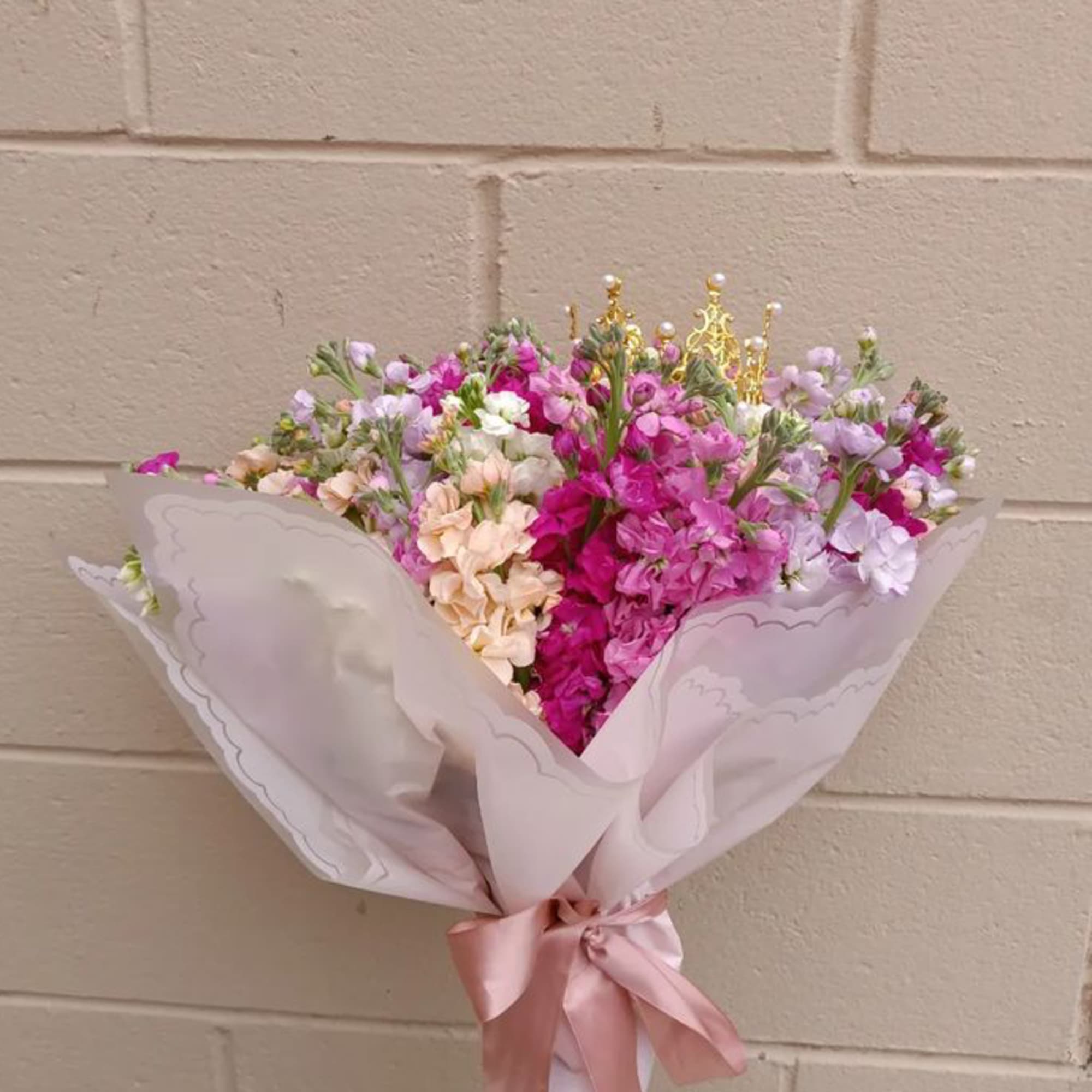 Bouquet of pink, lavender, and peach flowers wrapped in pale paper with a satin ribbon