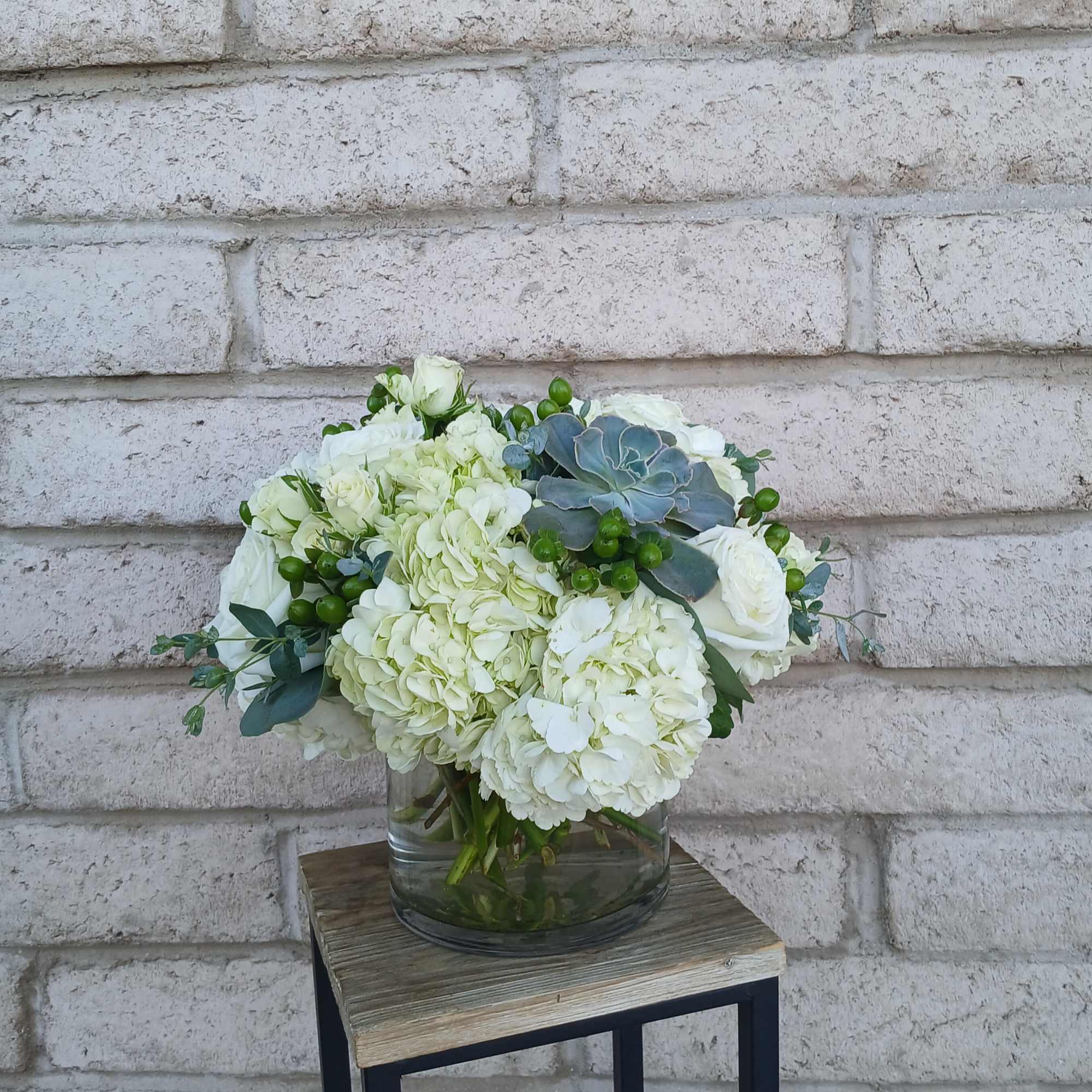 White floral arrangement in a glass vase with green accents