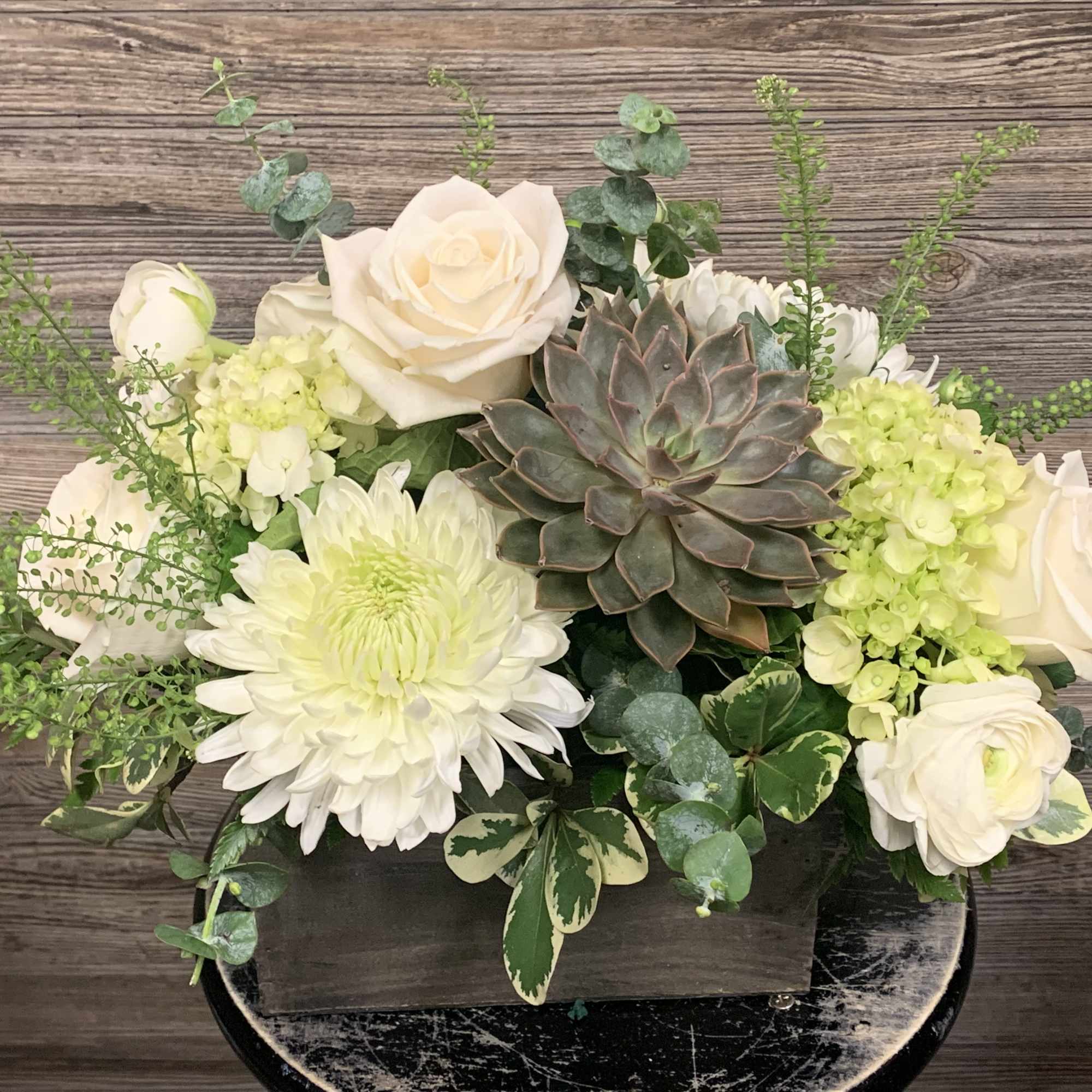 White roses and chrysanthemums arranged with a succulent in a dark container