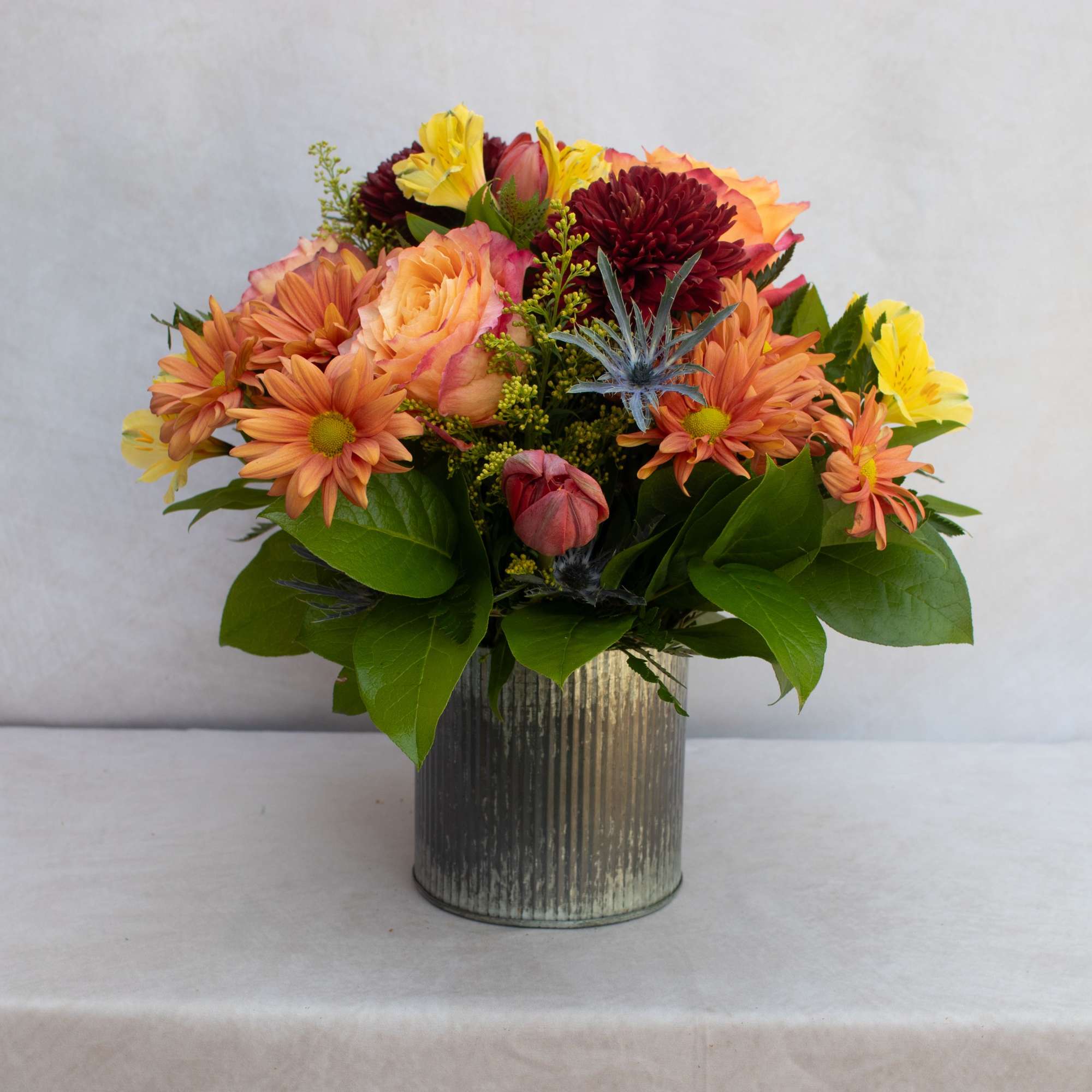 Mixed orange, yellow, and burgundy flowers in a ribbed metal vase